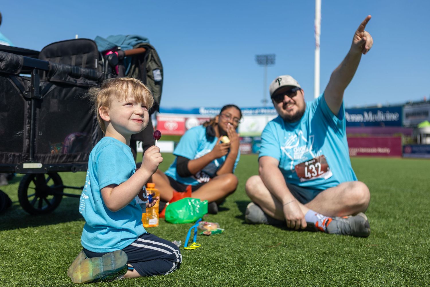 Participants in light blue shirts enjoy refreshments while sitting on grass at outdoor sporting event.