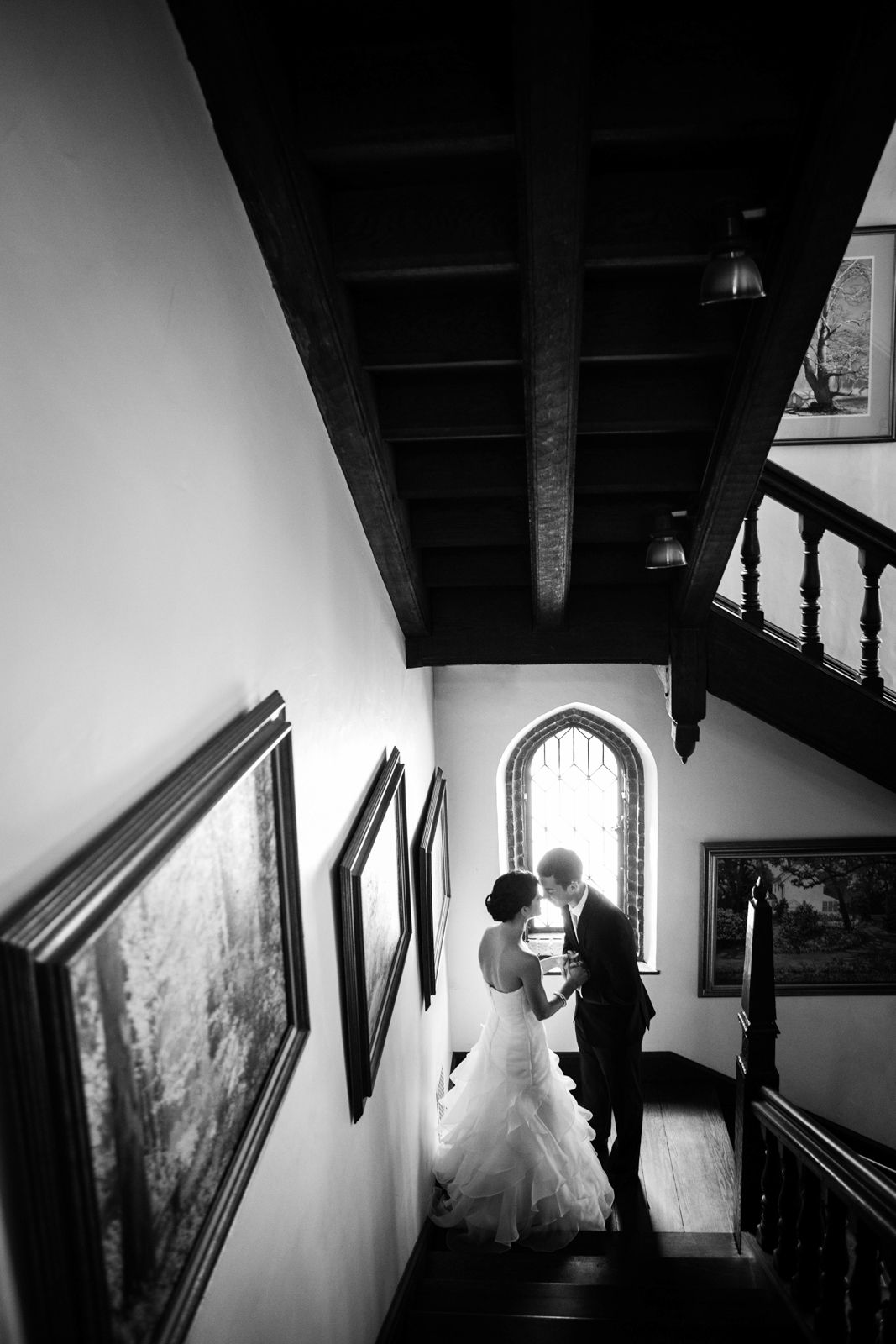 A silhouetted couple stands at the top of an elegant staircase with artwork on the walls in black and white photography.