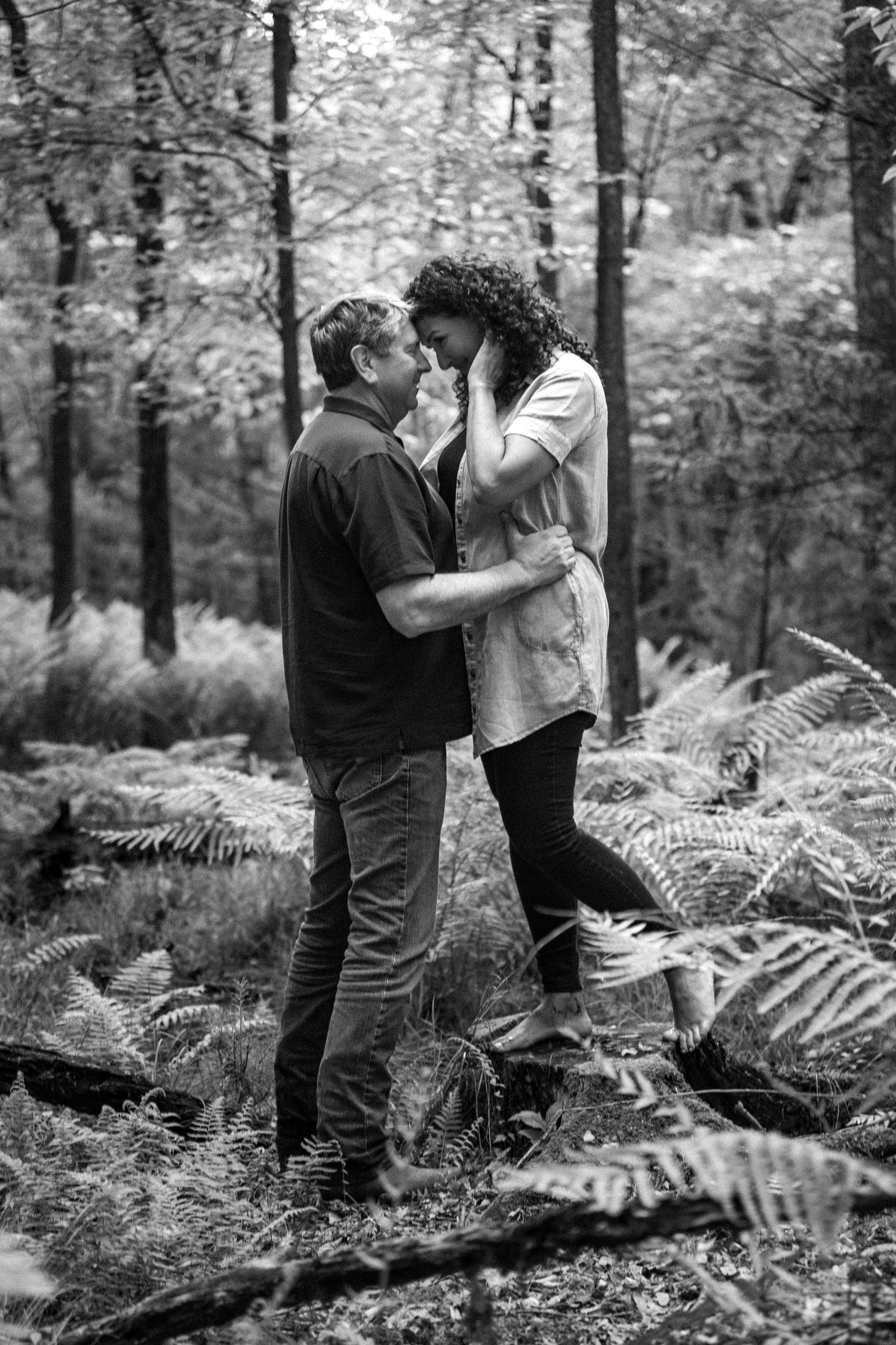 Romantic black and white photo of a couple sharing an intimate moment among ferns in a misty forest setting.
