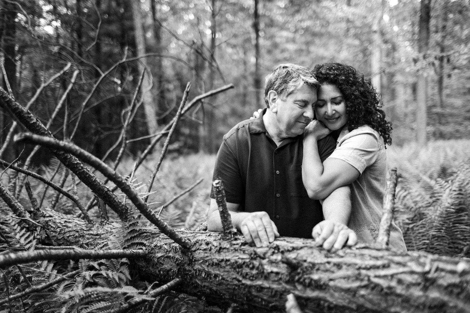 A couple shares an intimate moment together while sitting among ferns in a black and white forest setting.