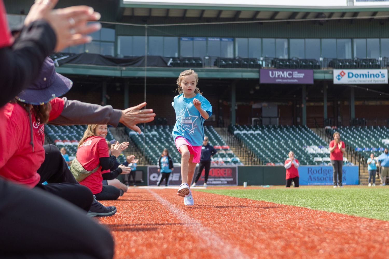A participant runs along the warning track at a baseball stadium while spectators cheer.