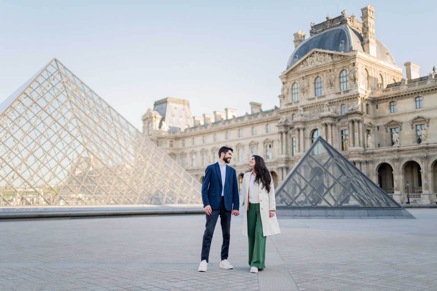 A couple stands in front of the iconic Louvre pyramid in Paris.