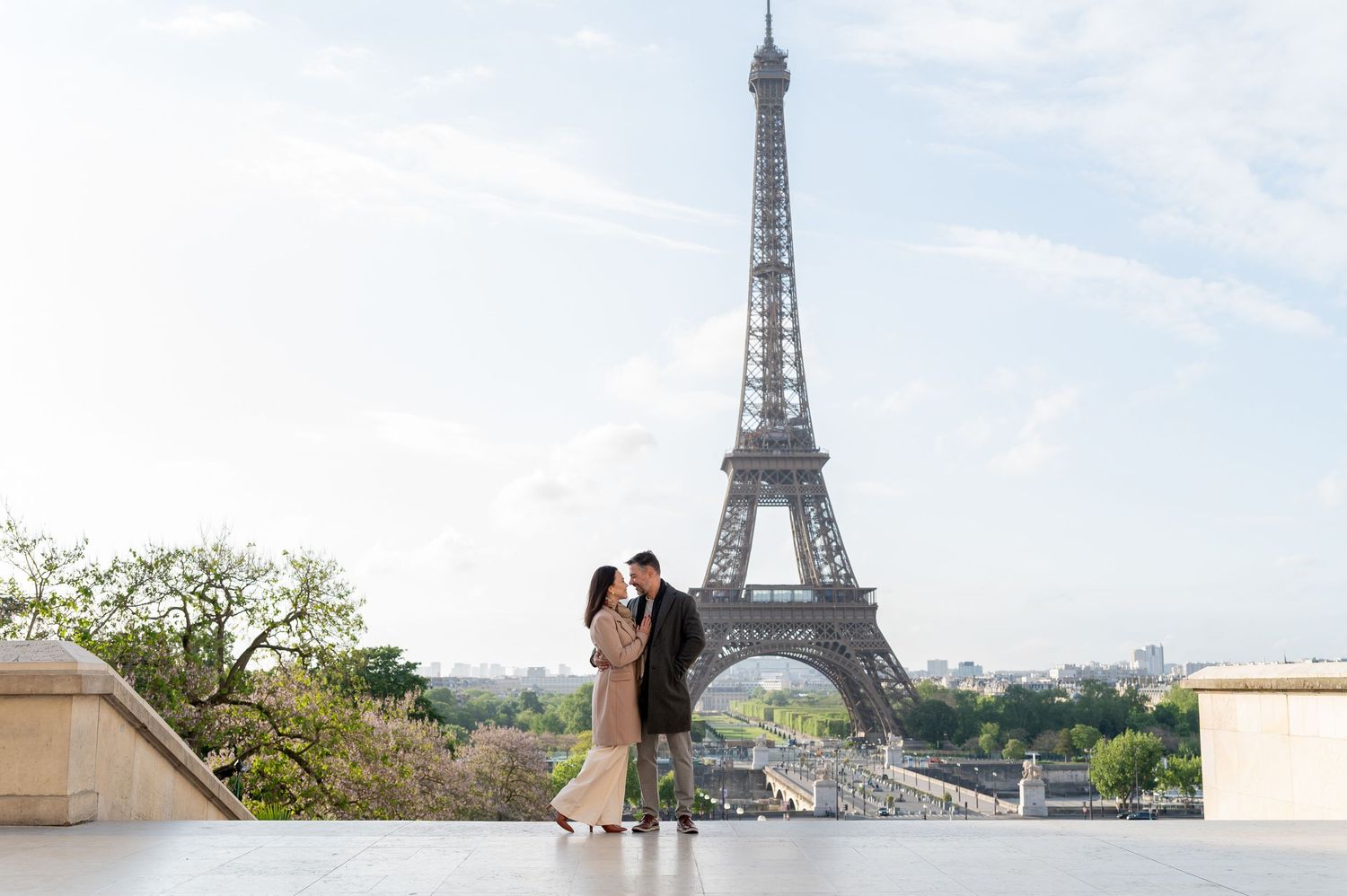 A couple embraces on a terrace with the iconic Eiffel Tower rising majestically in the background in Paris, France.