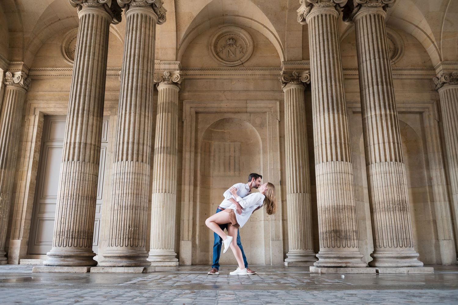 Dancers perform romantic dip pose among grand classical columns in ornate stone archway.