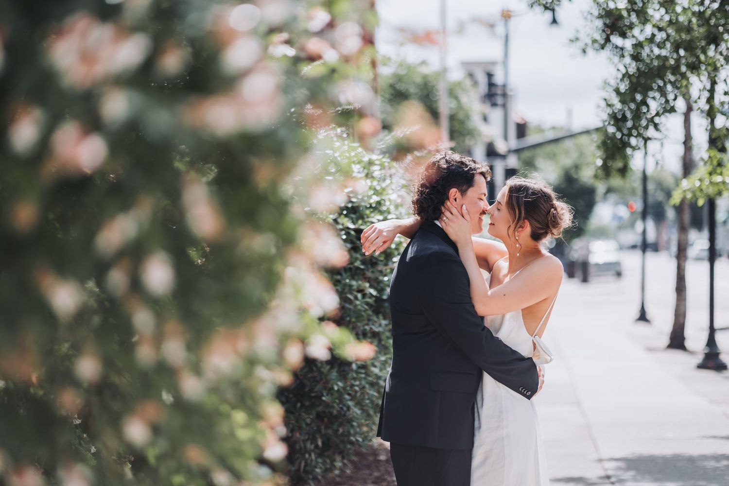 A romantic wedding couple embraces outdoors during a winter snow scene with street lights and buildings in the background.