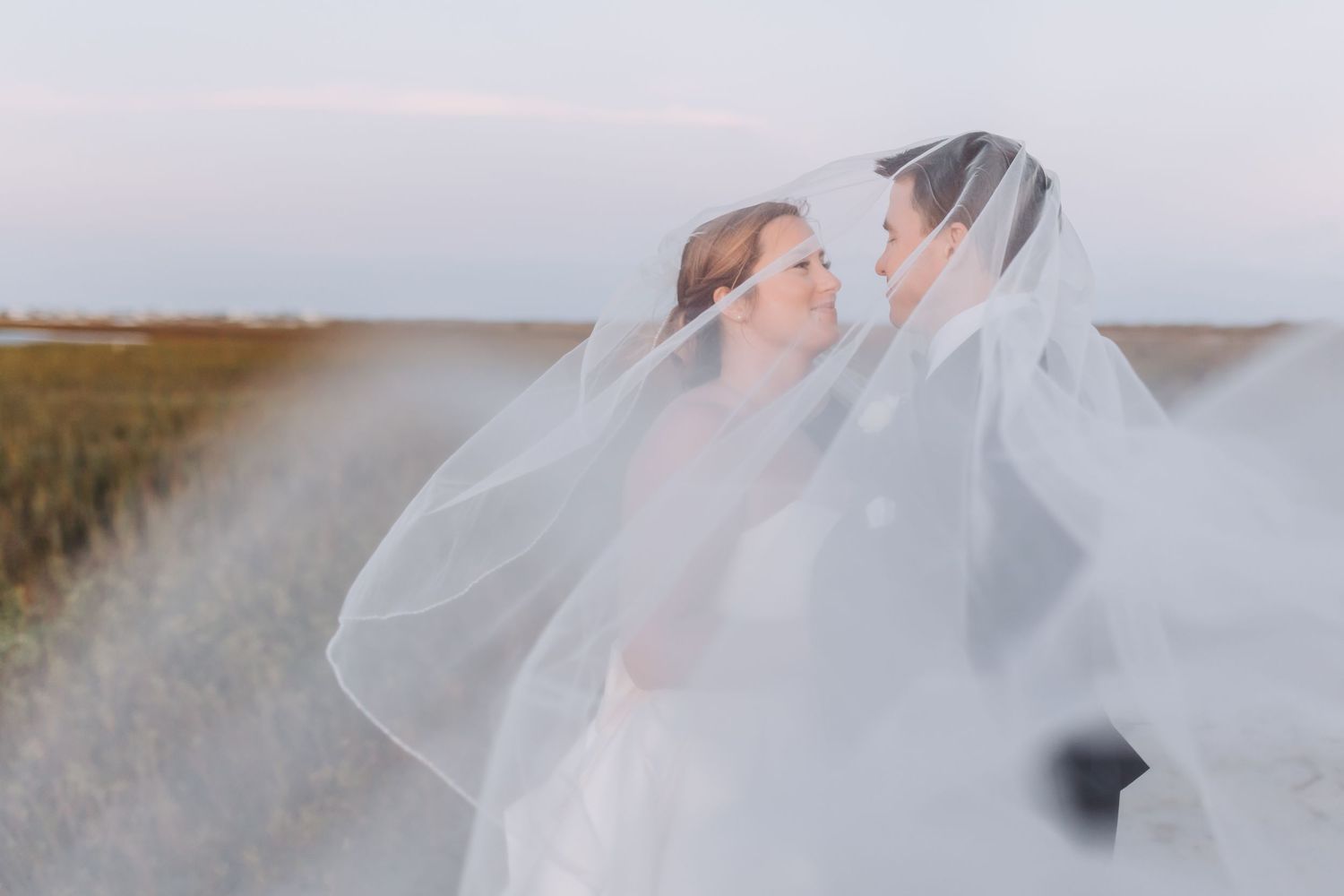 Two figures share a romantic moment in a field with white flowing fabric and grass in the background.