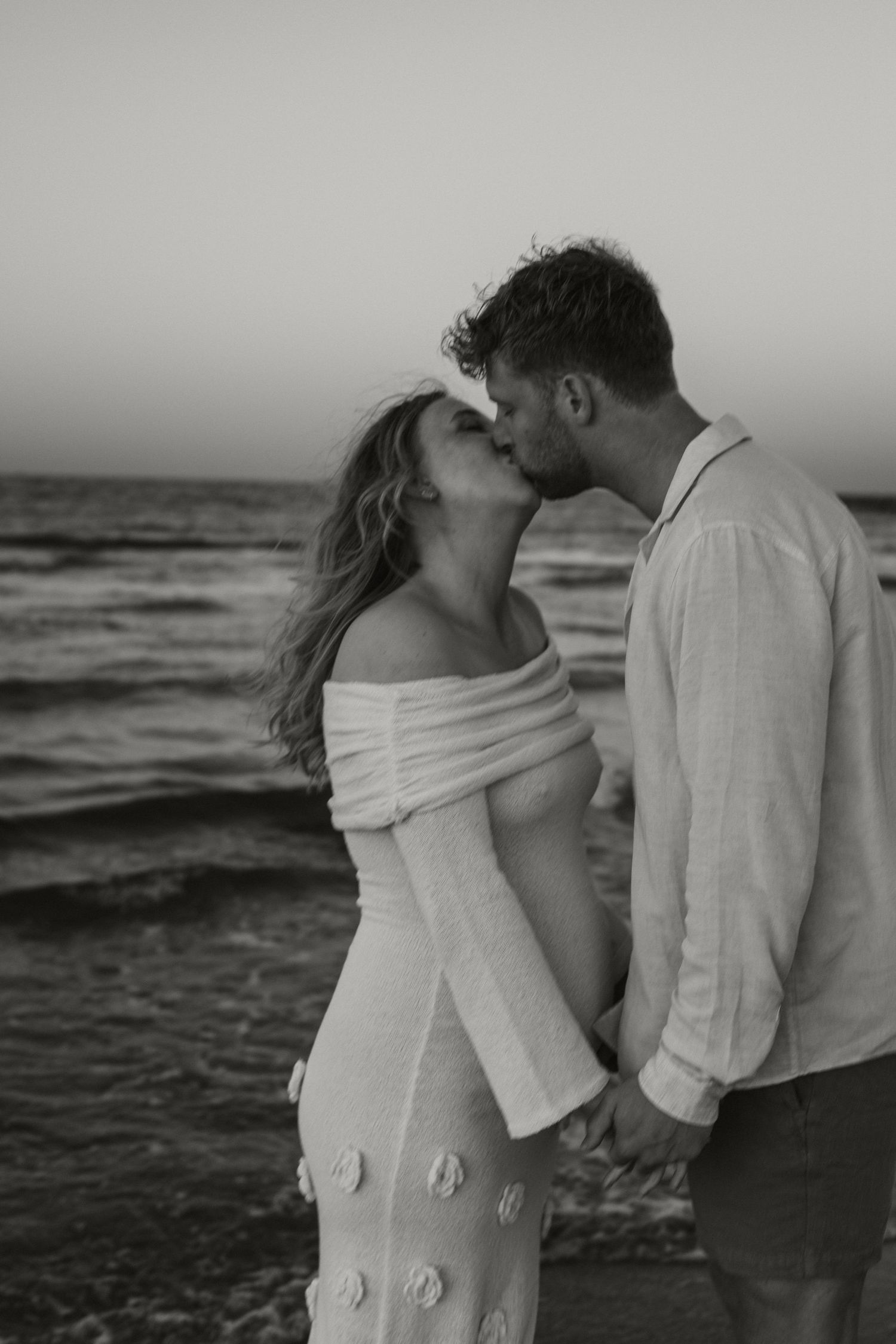 A romantic black and white beach photo of a couple sharing an intimate moment at sunset during a maternity session with a Photographer Javea