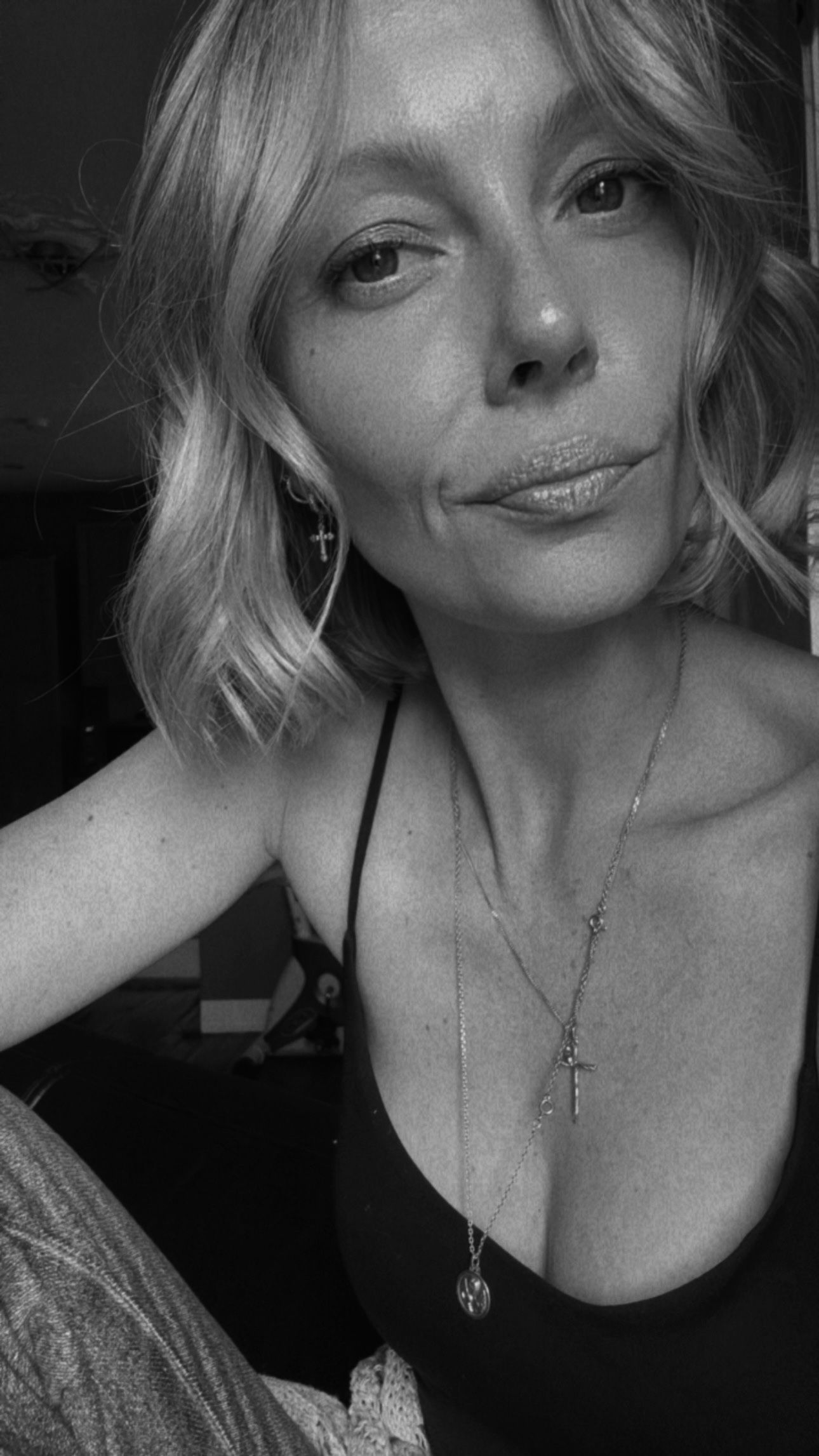 Black and white close-up portrait of a blonde woman wearing a dark top and cross necklace. Photographer Javea