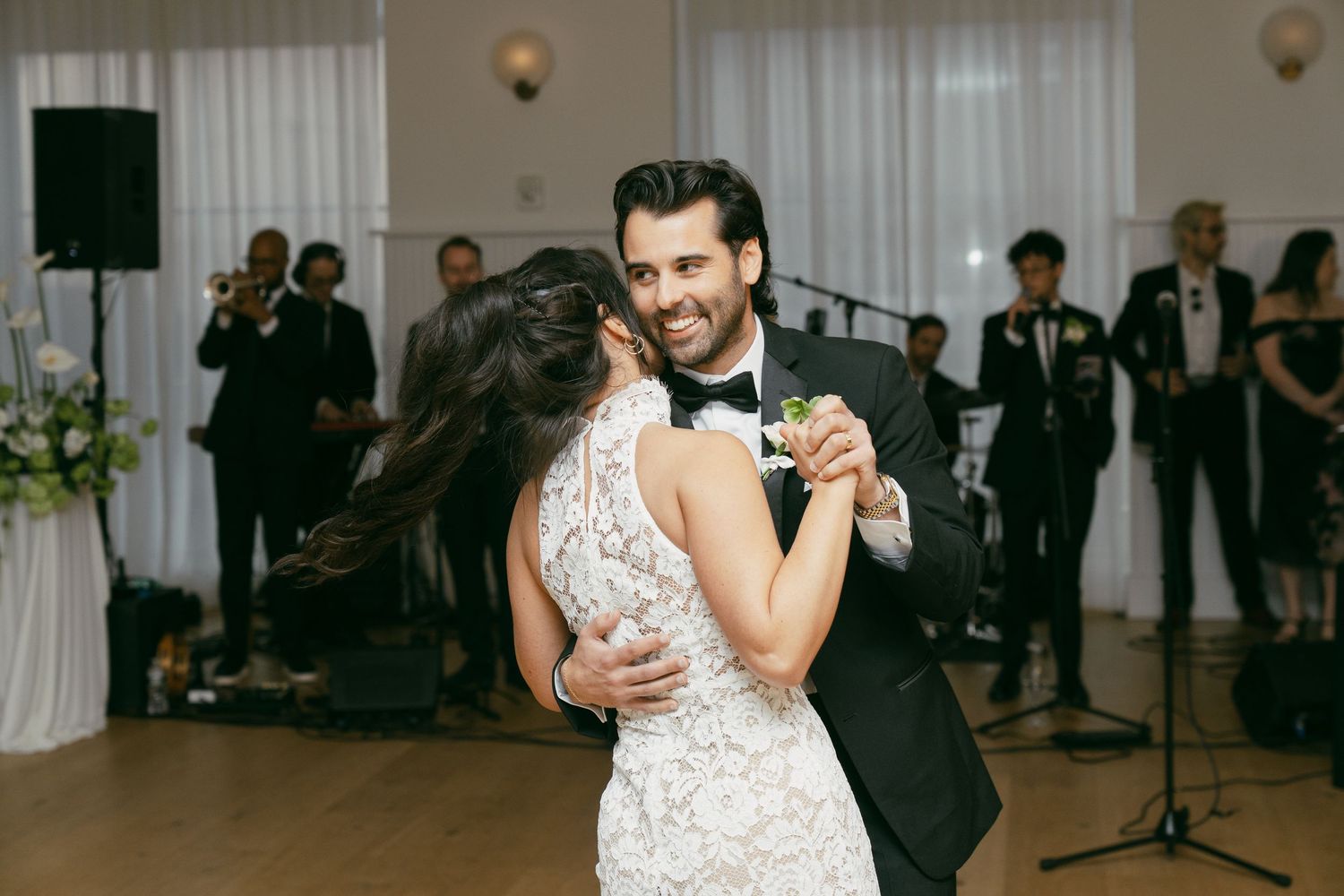 Couple dancing together at an elegant reception with band members visible in the background.
