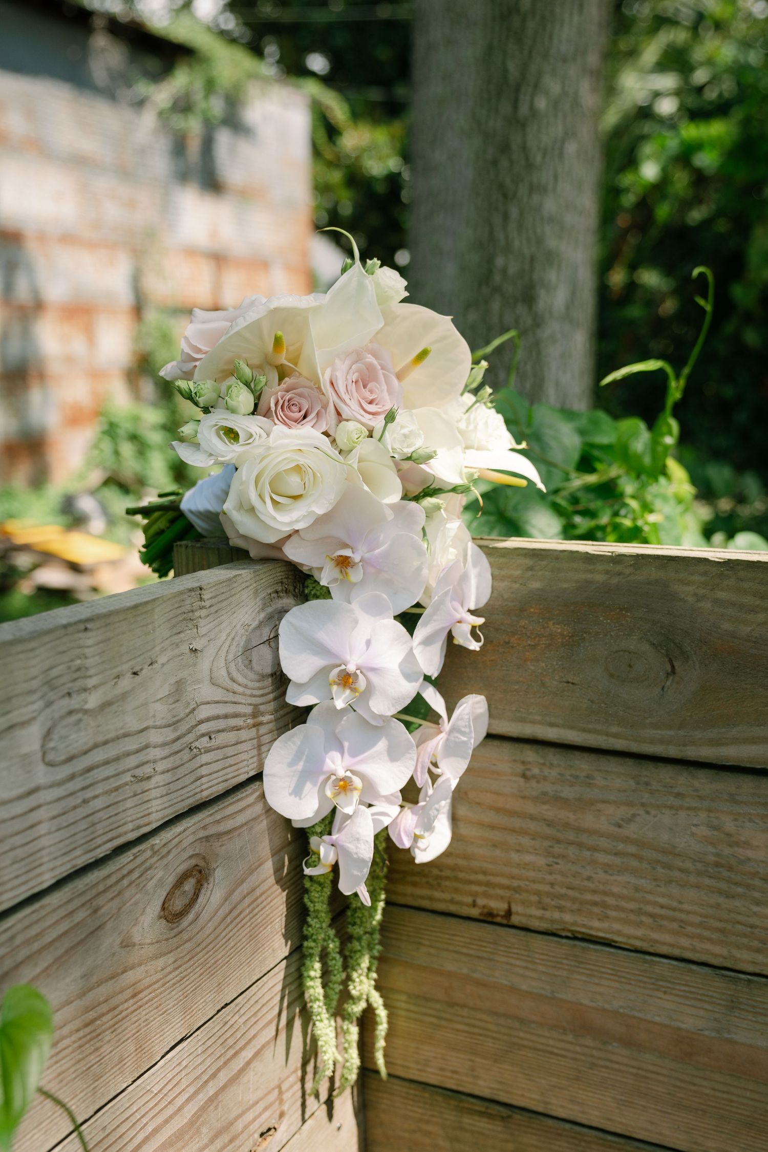 Elegant white and pink bridal bouquet with orchids and roses resting on wooden deck.