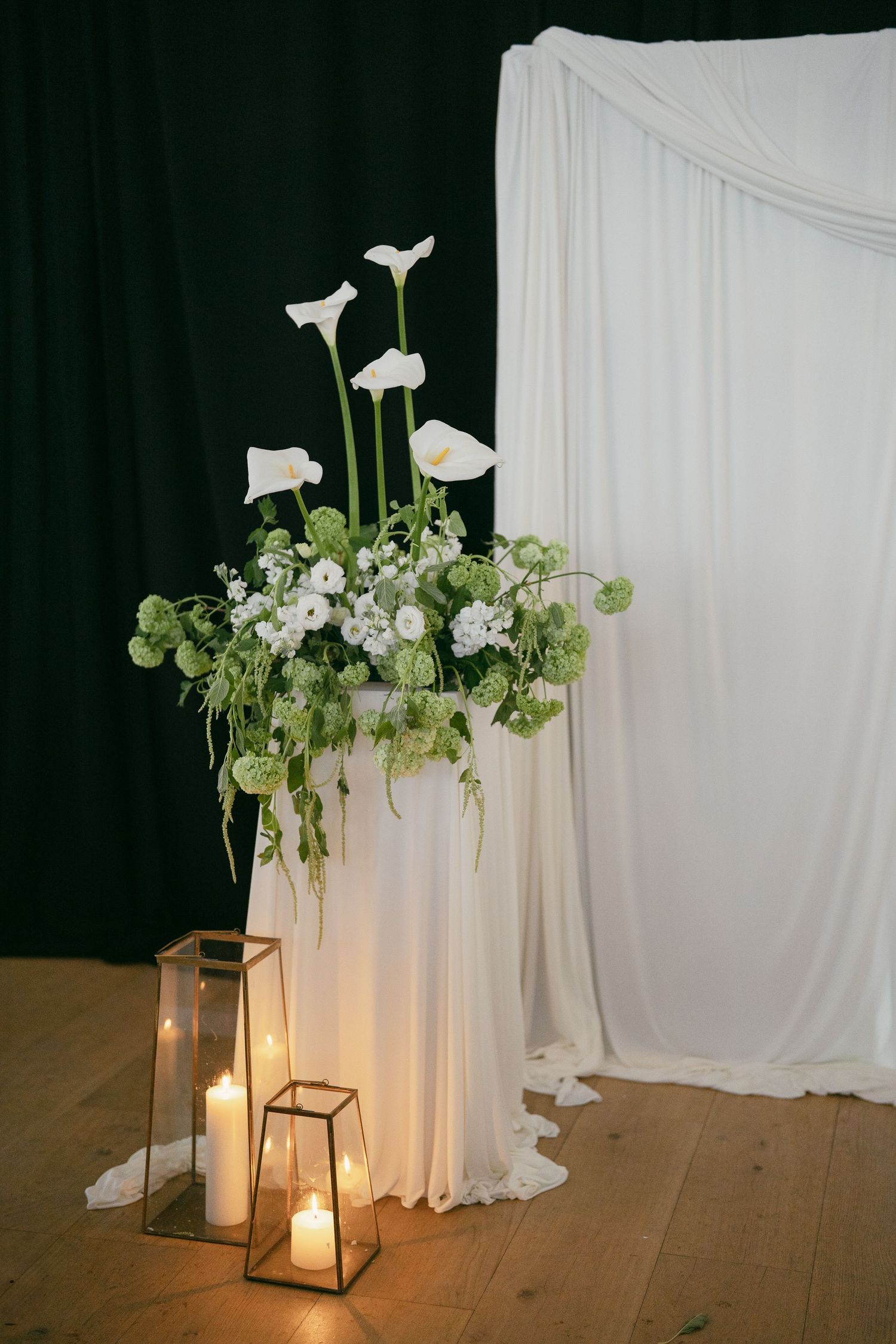 Modern minimalist wedding decor featuring white calla lilies and lanterns against white draping.