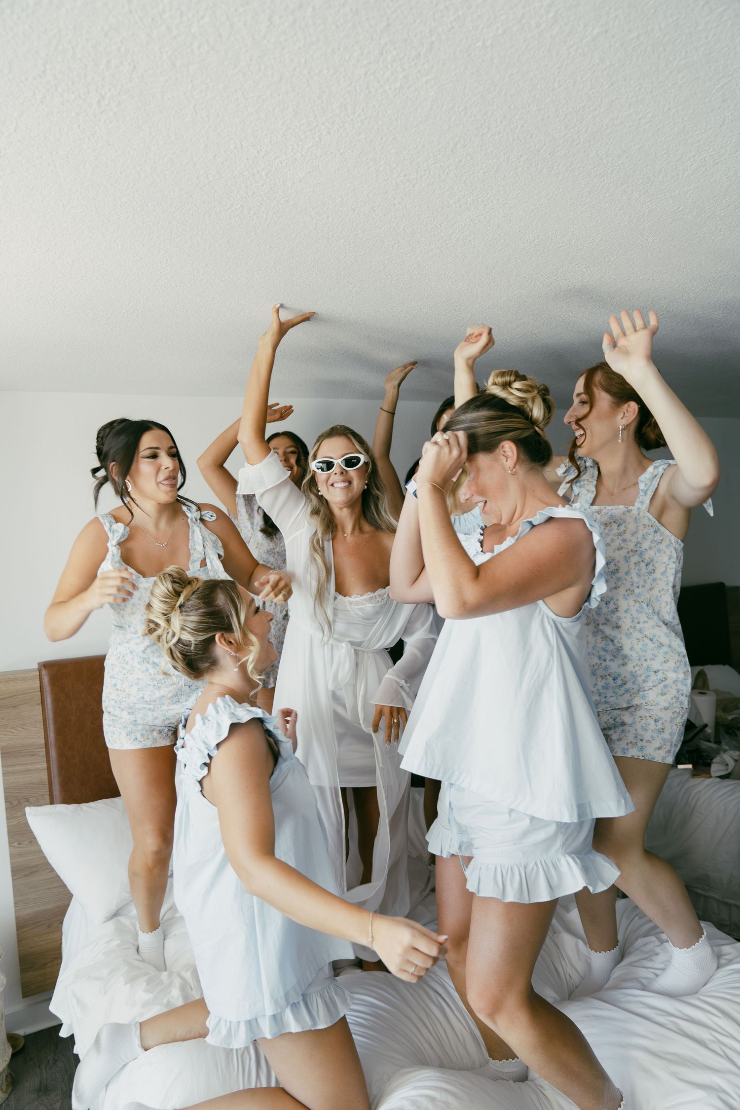 A group of women in white outfits jumping and dancing on a bed during a celebration.