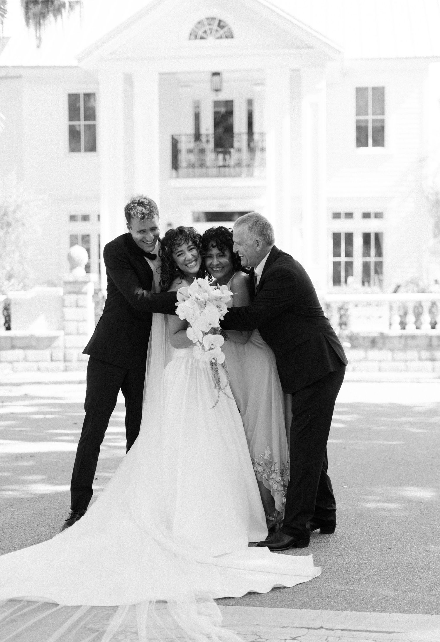 A joyful wedding portrait taken in front of a classic white Southern mansion.