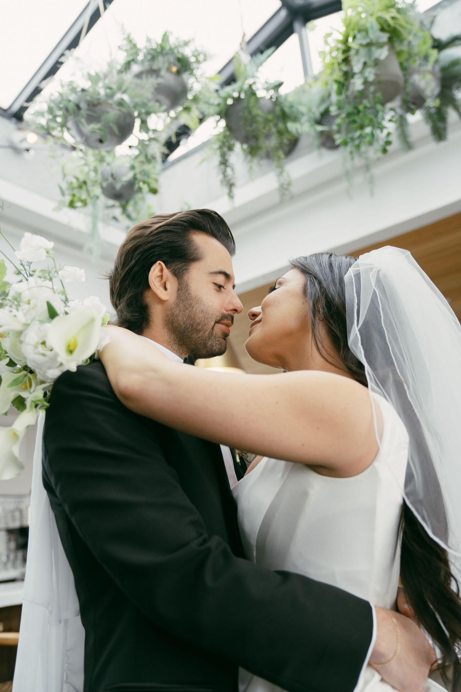 Romantic wedding moment under floral ceiling decorations in an indoor venue.