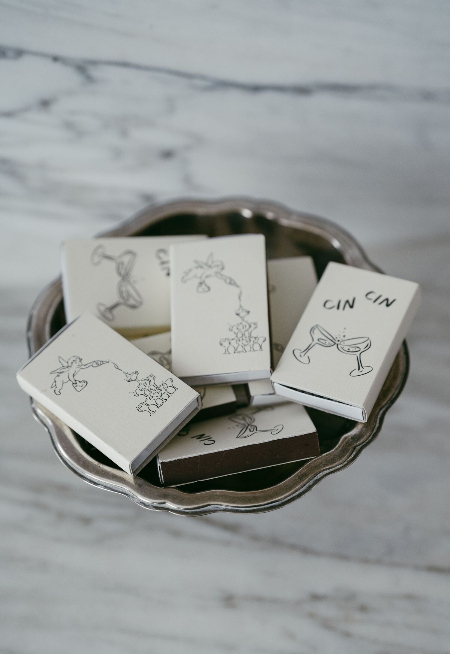 Decorative silver plate holding small cards with hand-drawn stick figure illustrations on a marble surface.