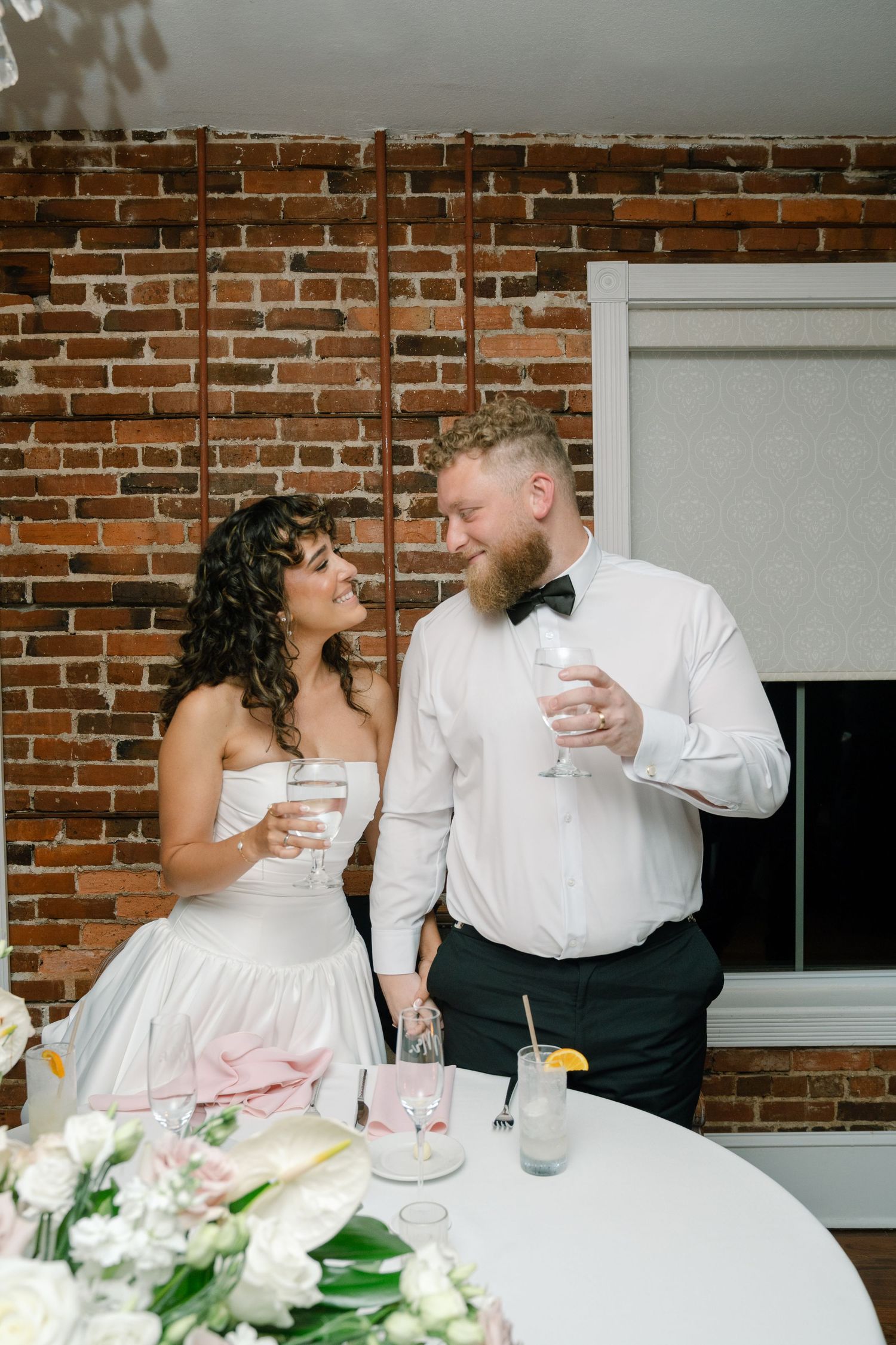 Wedding celebration toast against exposed brick wall with elegant white floral centerpiece.