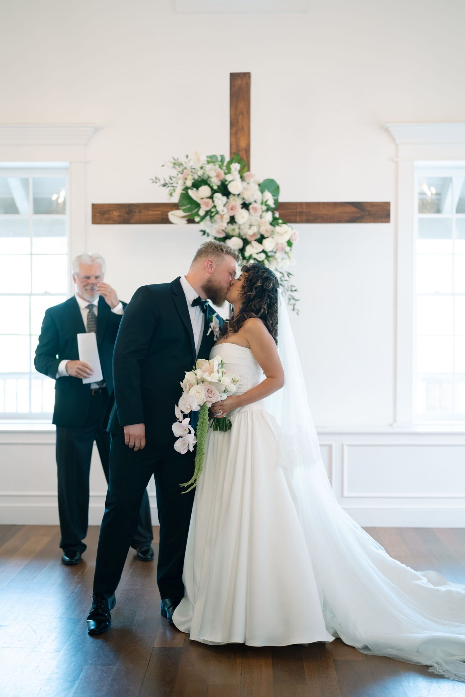 First look moment between newlyweds in a bright white venue with floral decorations.