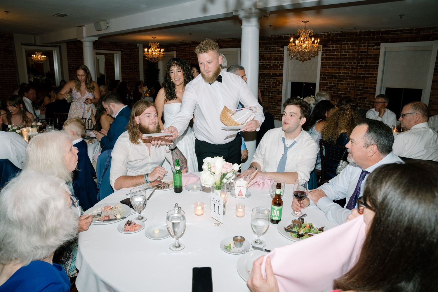 Wedding reception guests gather around white-clothed tables under crystal chandeliers.
