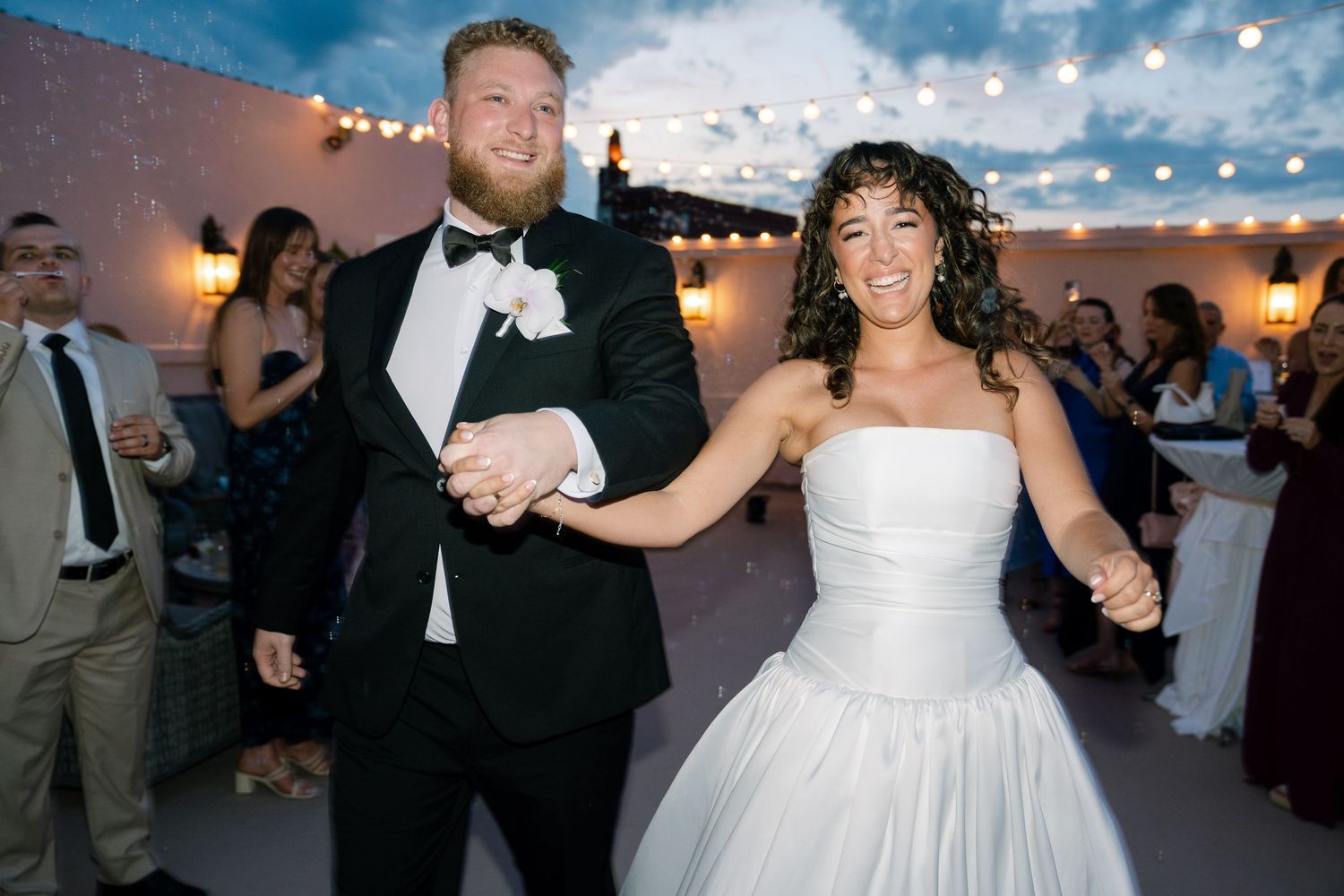Couple dances joyfully at their outdoor wedding reception under string lights at dusk.