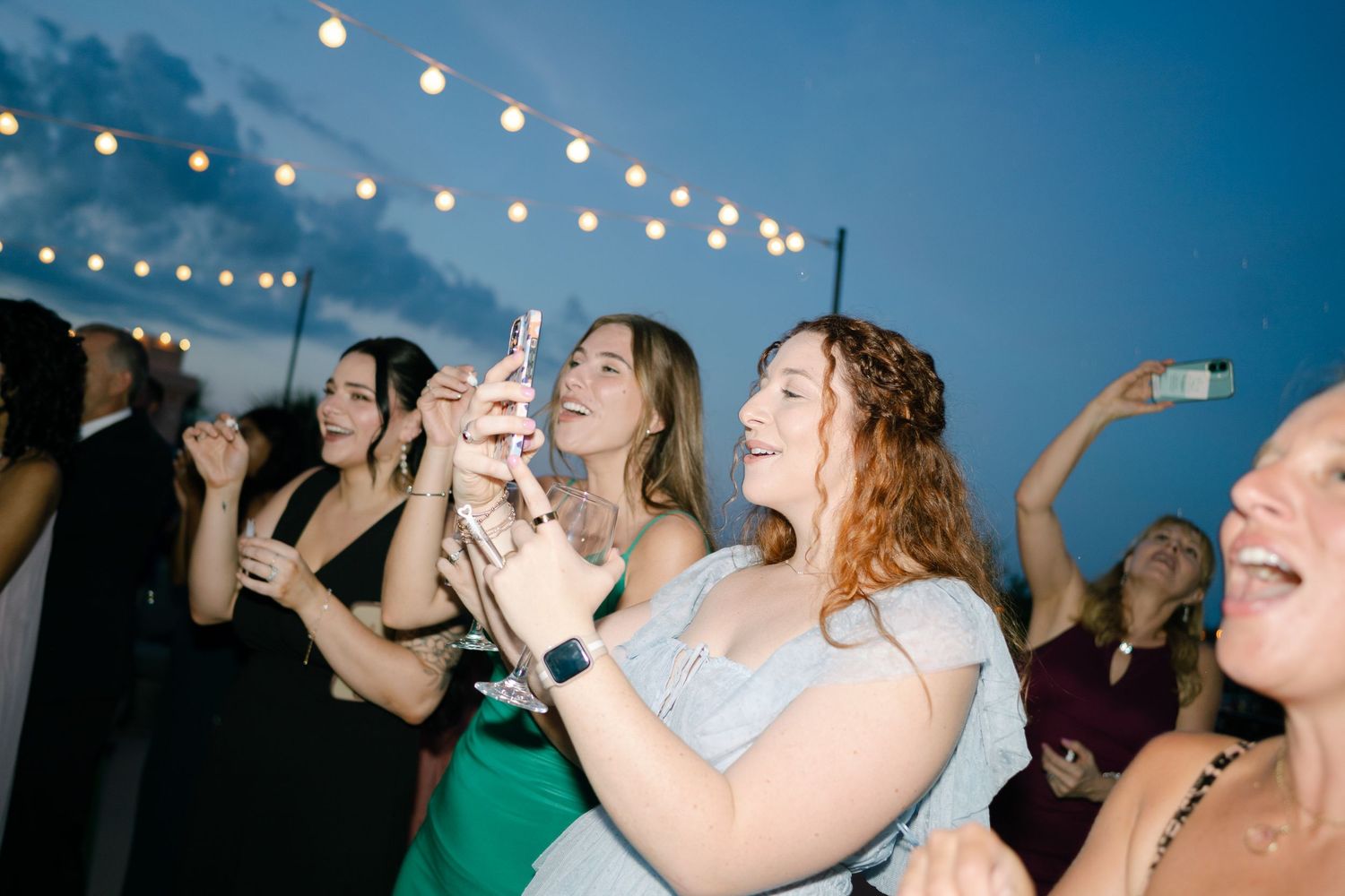 Wedding guests taking shots and celebrating during a lively reception under string lights.