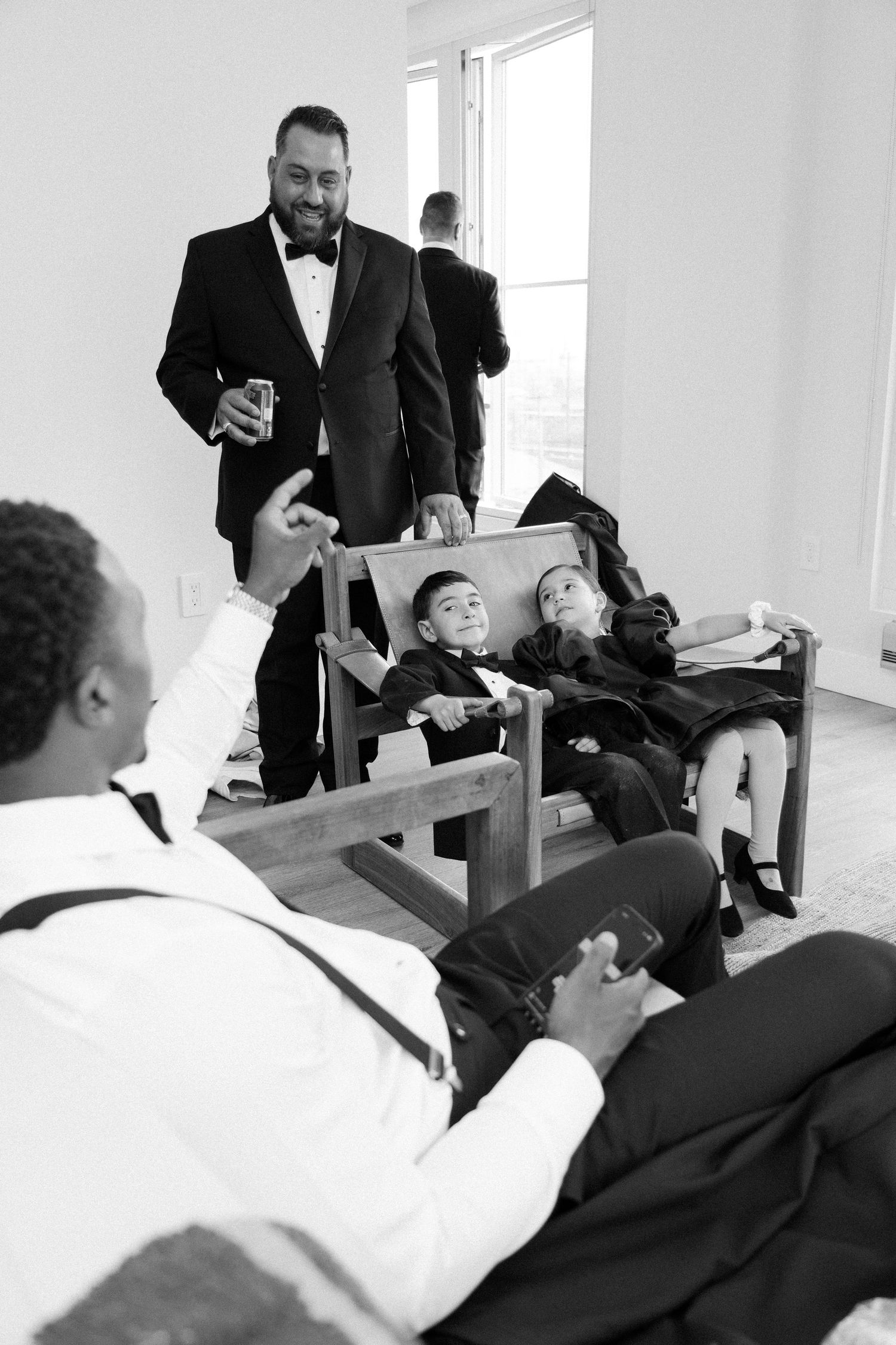 Black and white photo showing groomsmen relaxing and lounging with drinks during wedding preparations.