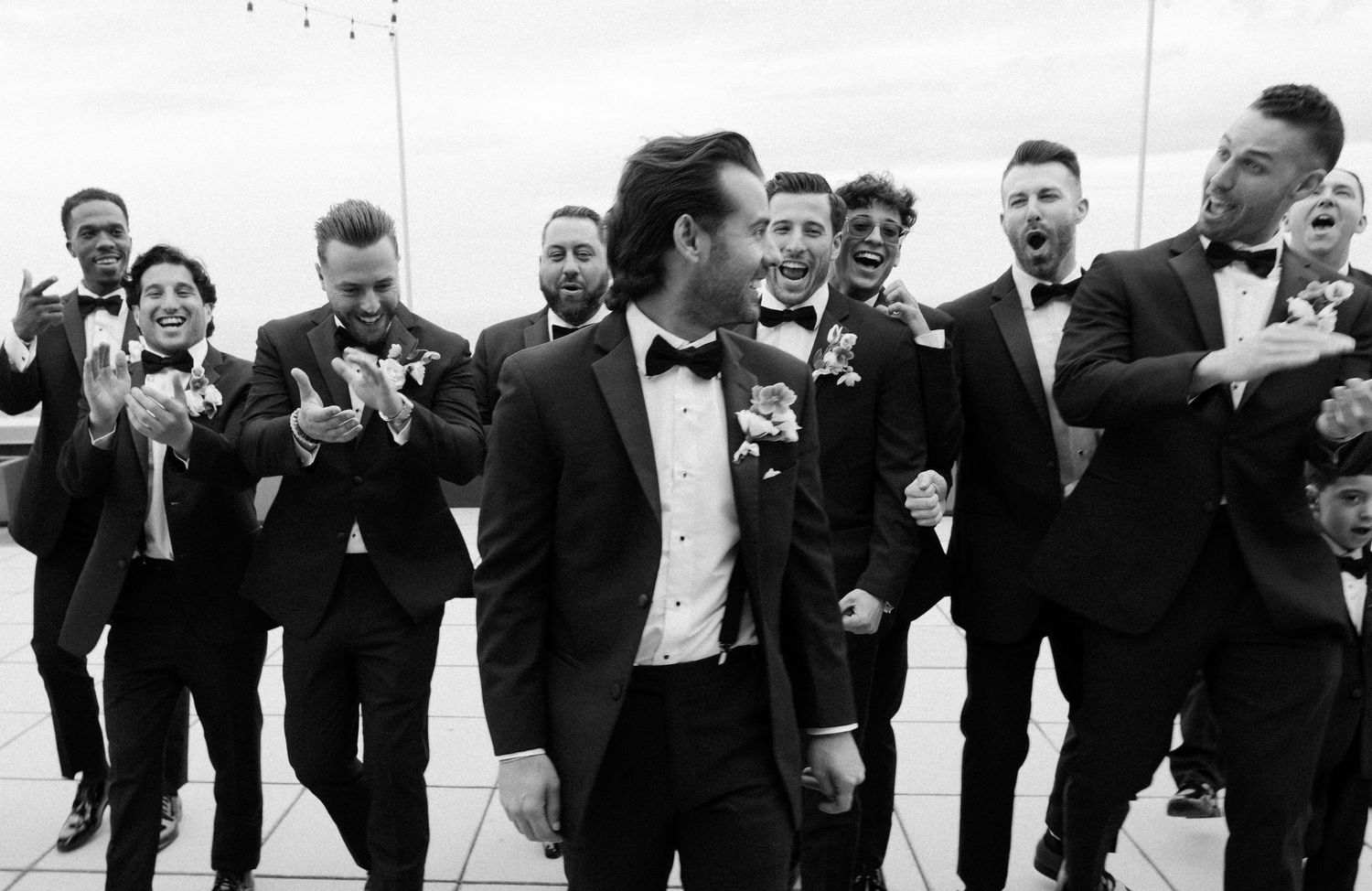 Groomsmen celebrate joyfully together in black tuxedos at a wedding.