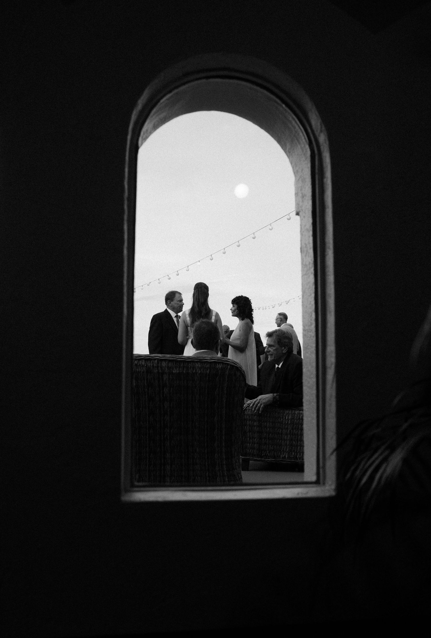 Silhouettes of wedding guests framed through an arched window in black and white.