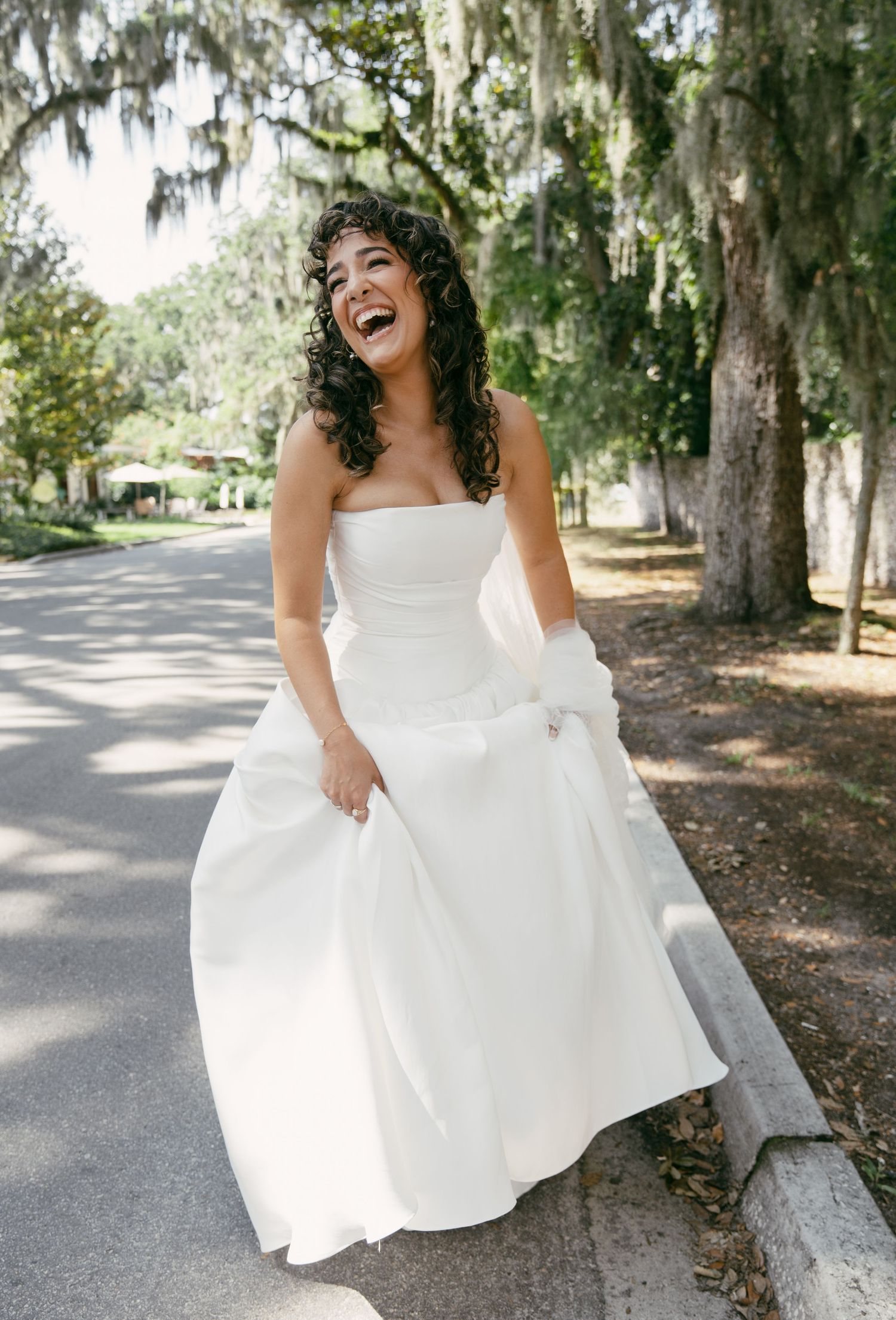 A joyful bridal portrait on a tree-lined Southern street with Spanish moss overhead.