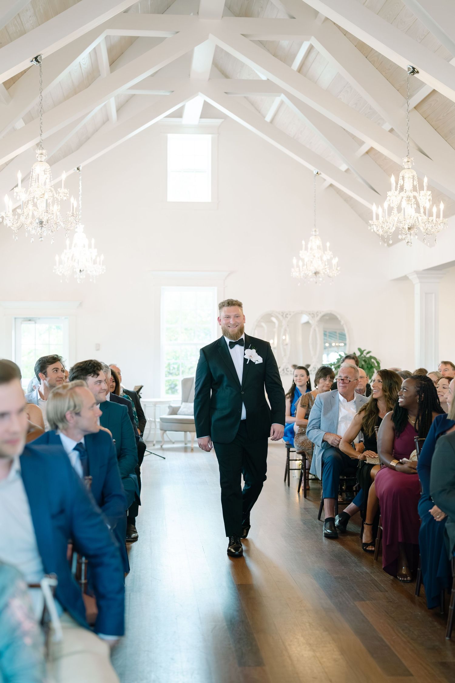 An elegant chapel interior with white beams and crystal chandeliers during a wedding ceremony.