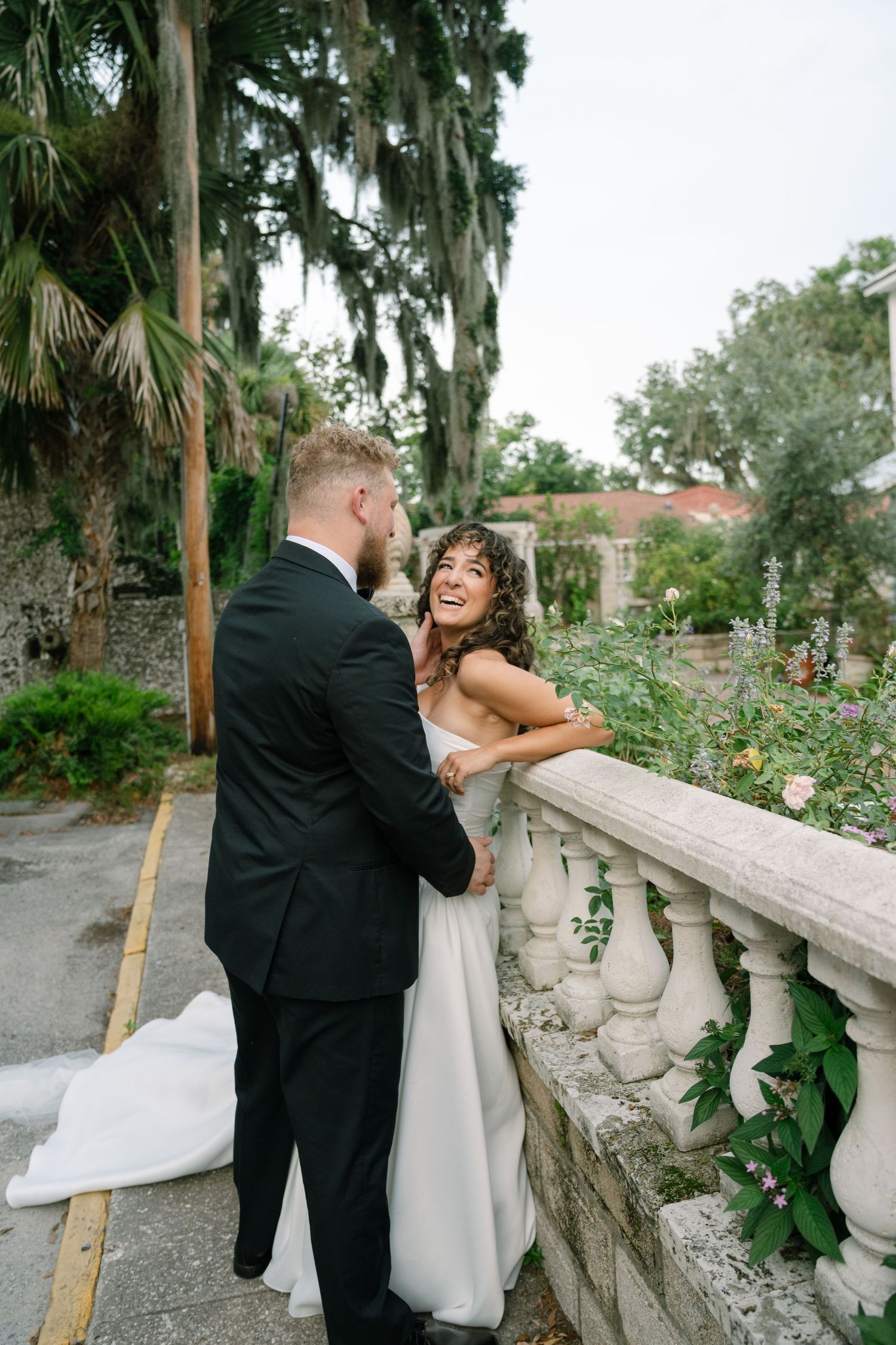Happy couple shares a joyful moment on a stone balcony surrounded by lush Southern garden.