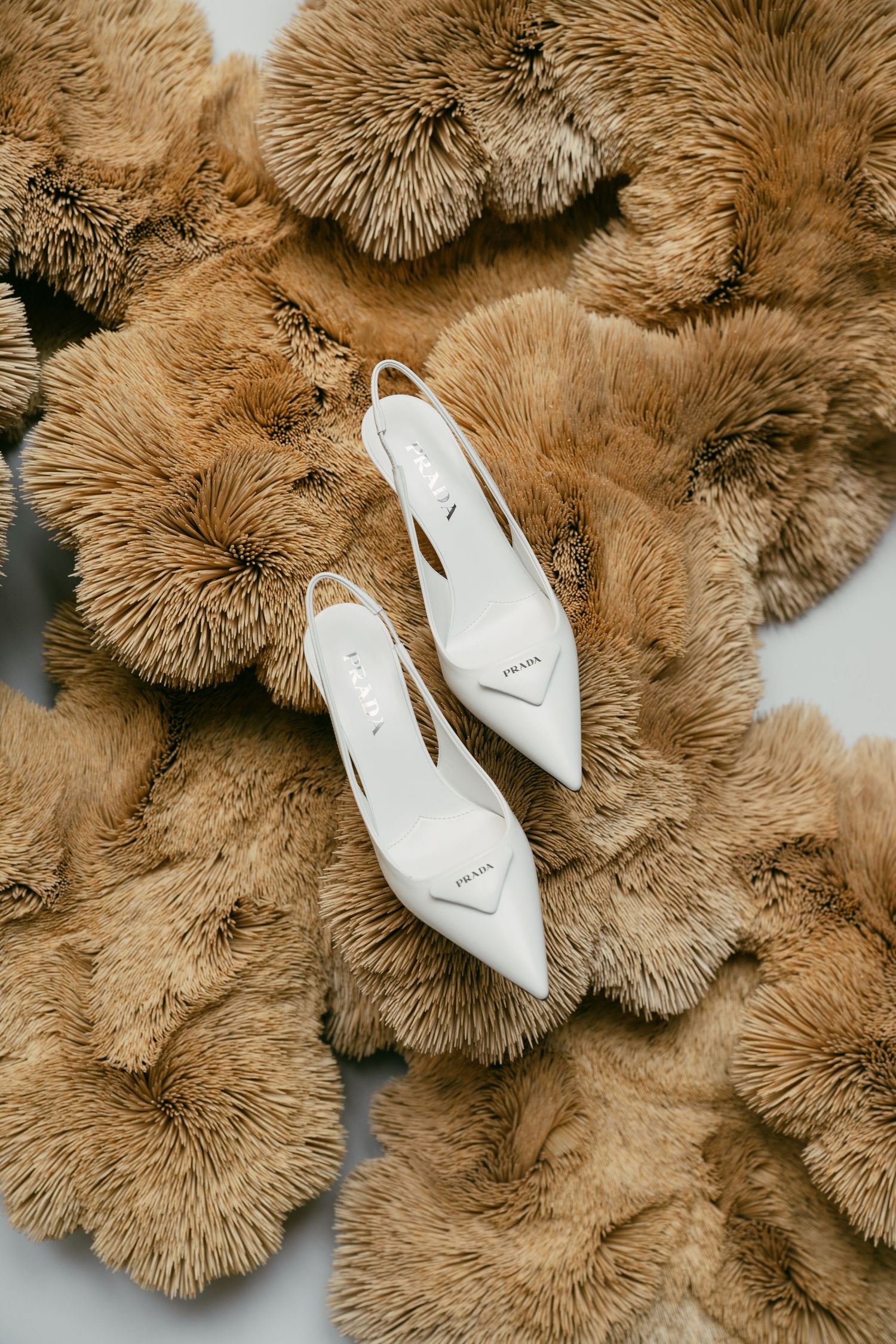 Elegant white bridal shoes placed on fluffy brown textured decor.