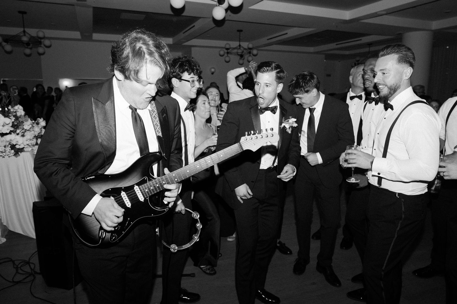 Wedding band performs with electric guitar as guests gather around during reception celebration.