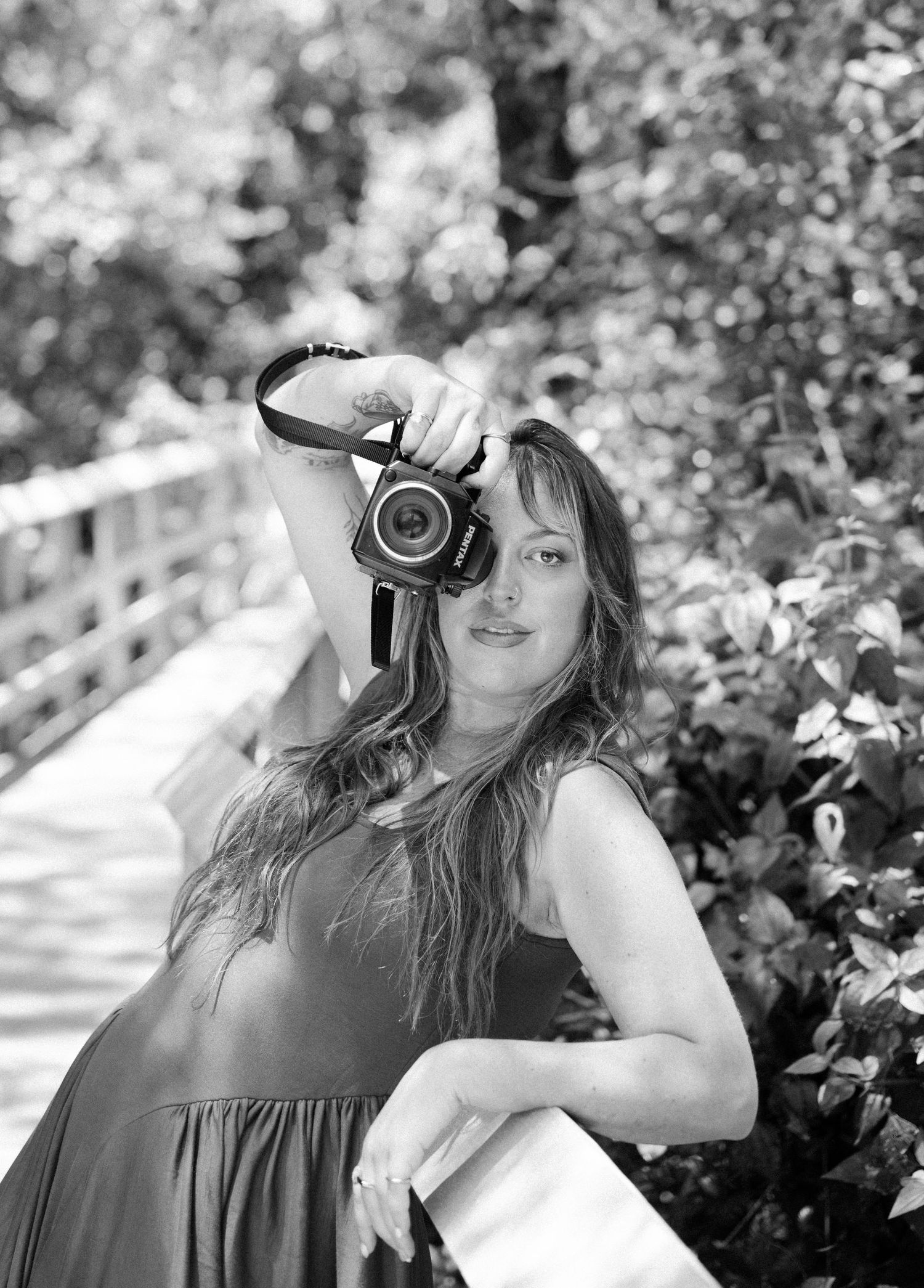 A photographer holds up a DSLR camera while standing outdoors in a black and white portrait.