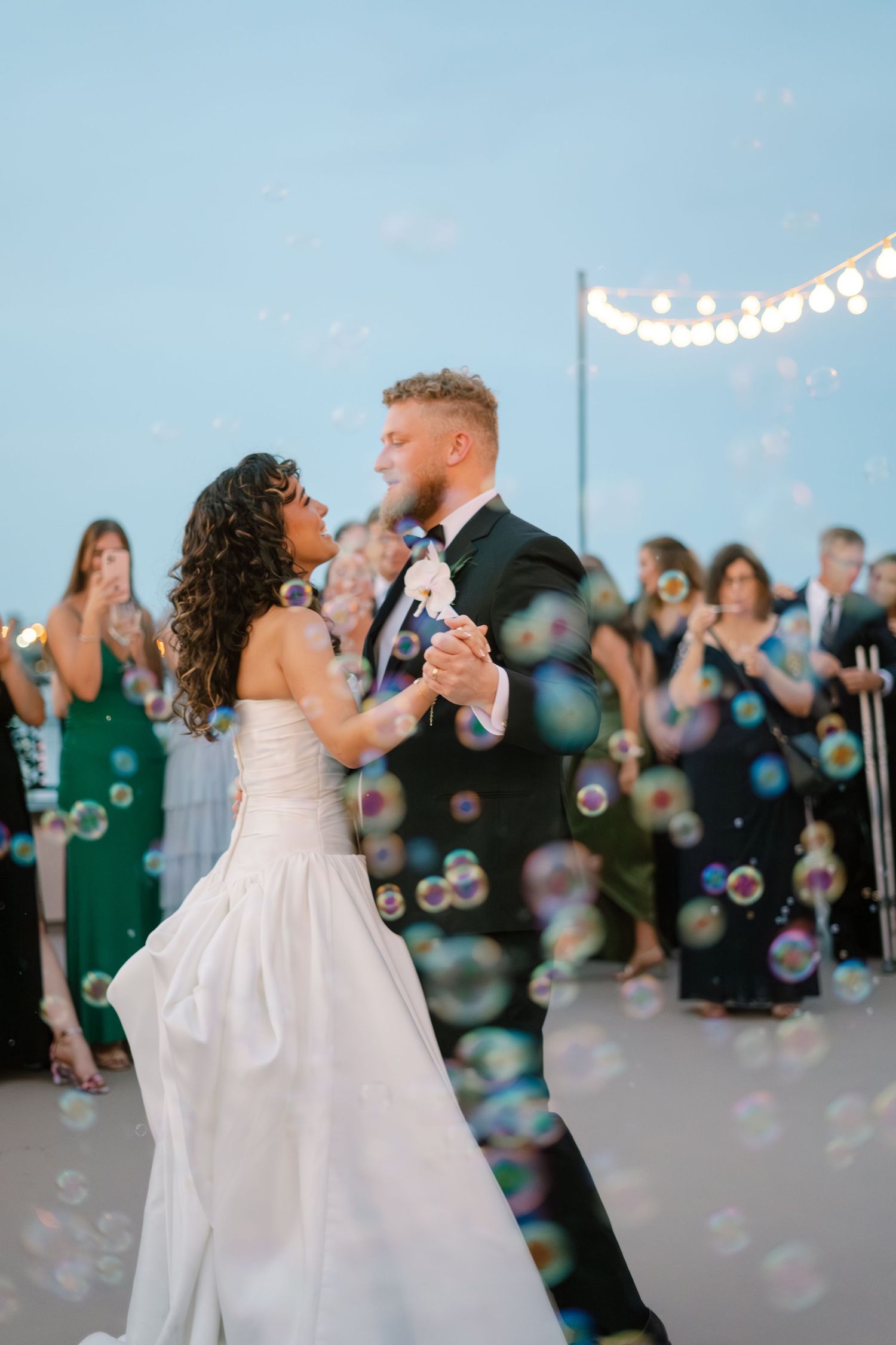 Wedding couple dancing surrounded by floating bubbles during sunset reception.