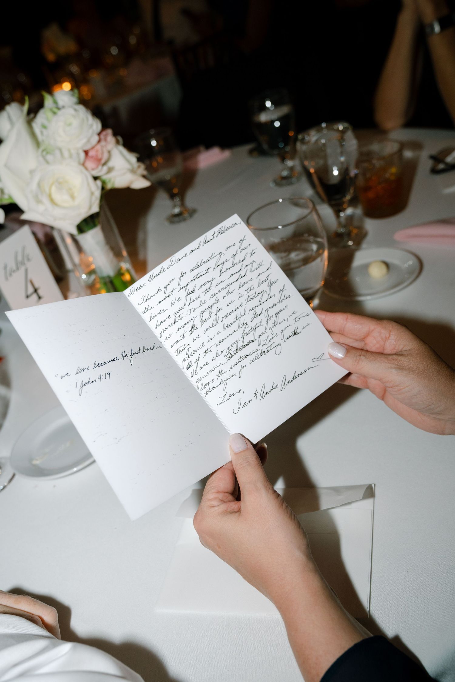 A handwritten note being read at an elegant wedding reception table setting.