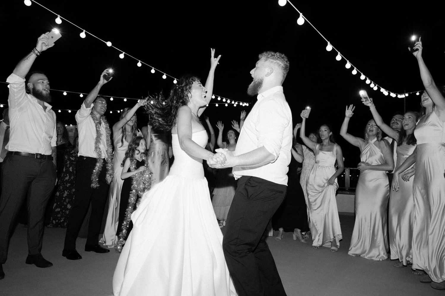Wedding reception dance floor under string lights with guests celebrating.