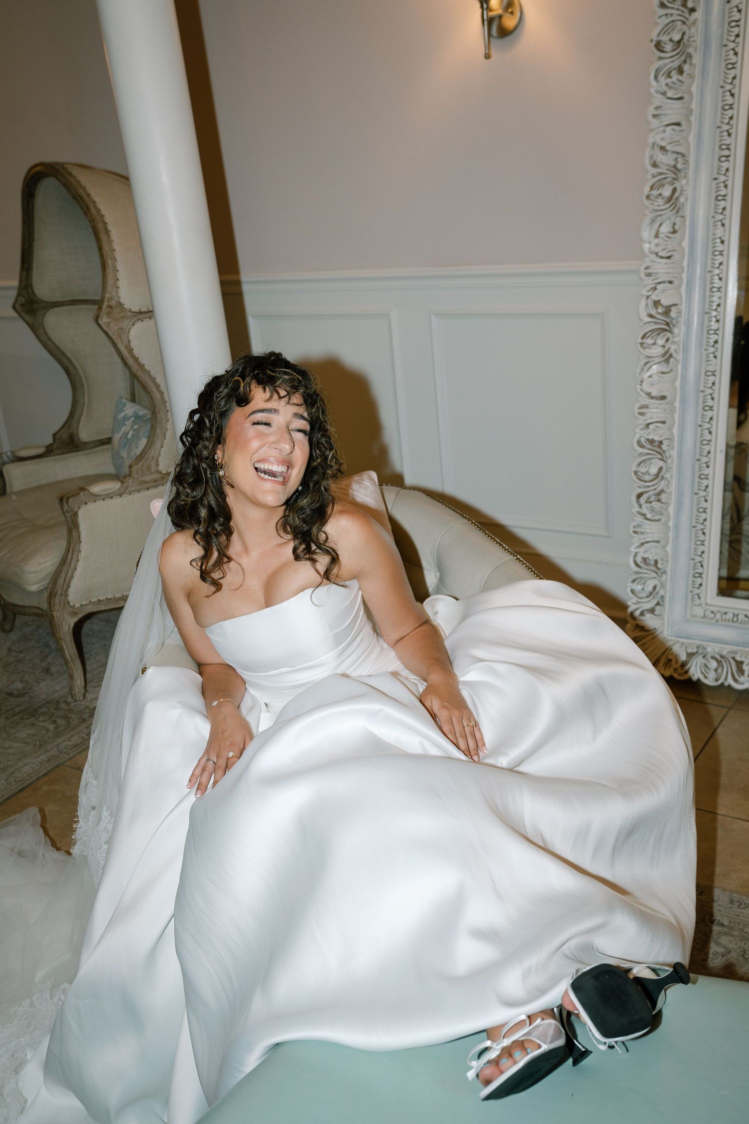 A bride in a white strapless wedding gown lounges on an elegant couch during her special day celebration.