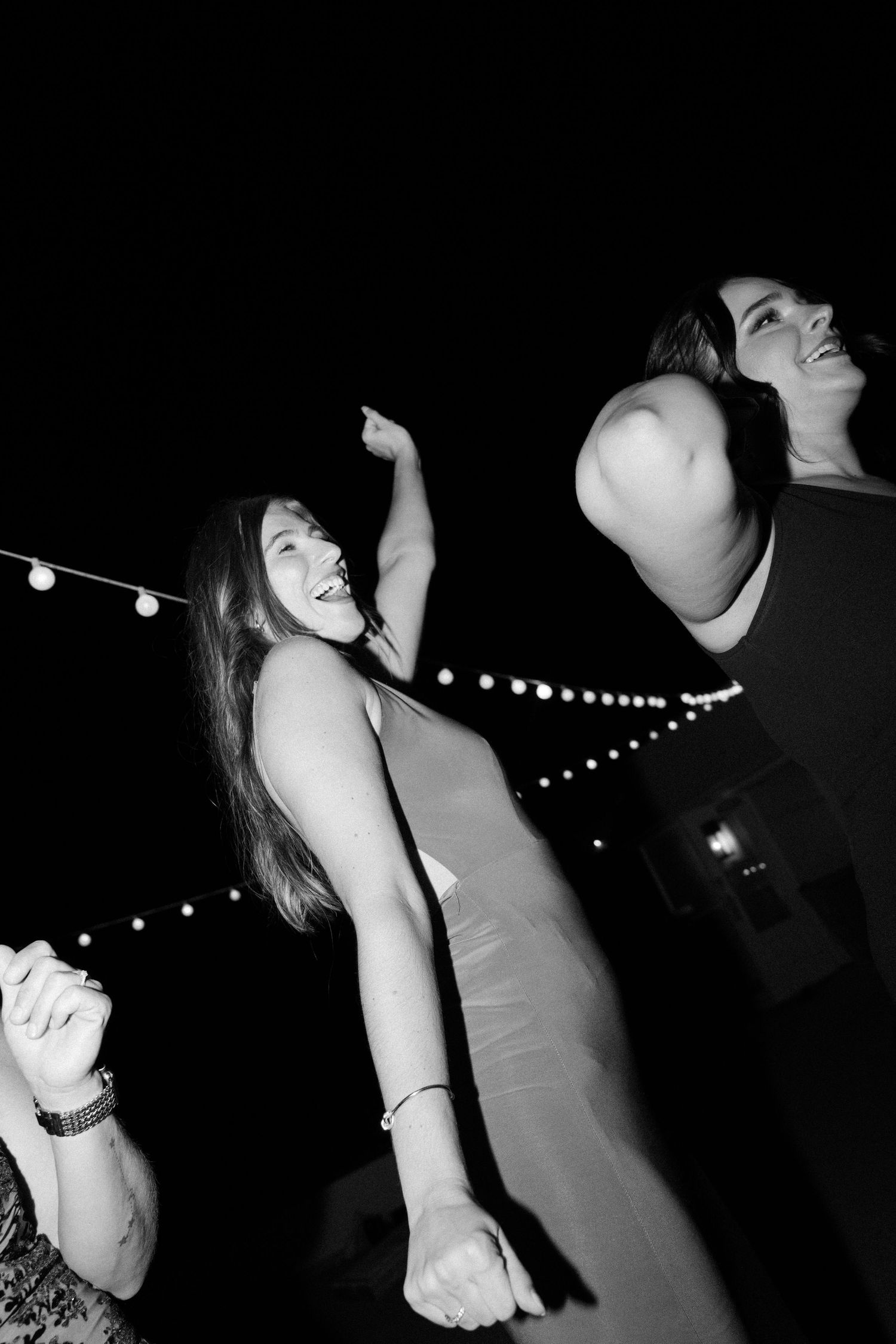 Black and white photo of people dancing under string lights at a nighttime celebration.