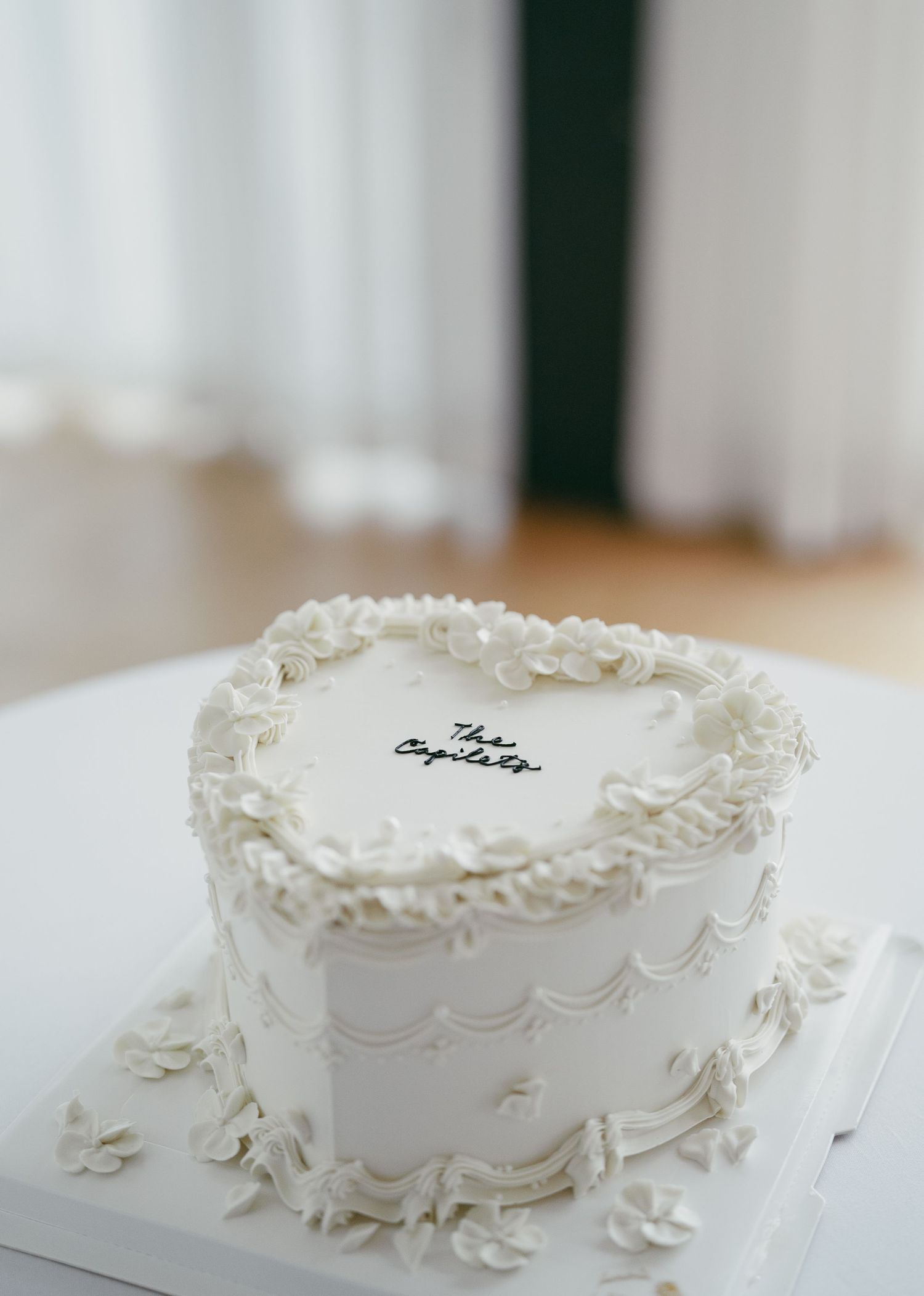 An elegant white wedding cake with delicate piped frosting details and scalloped decorations.