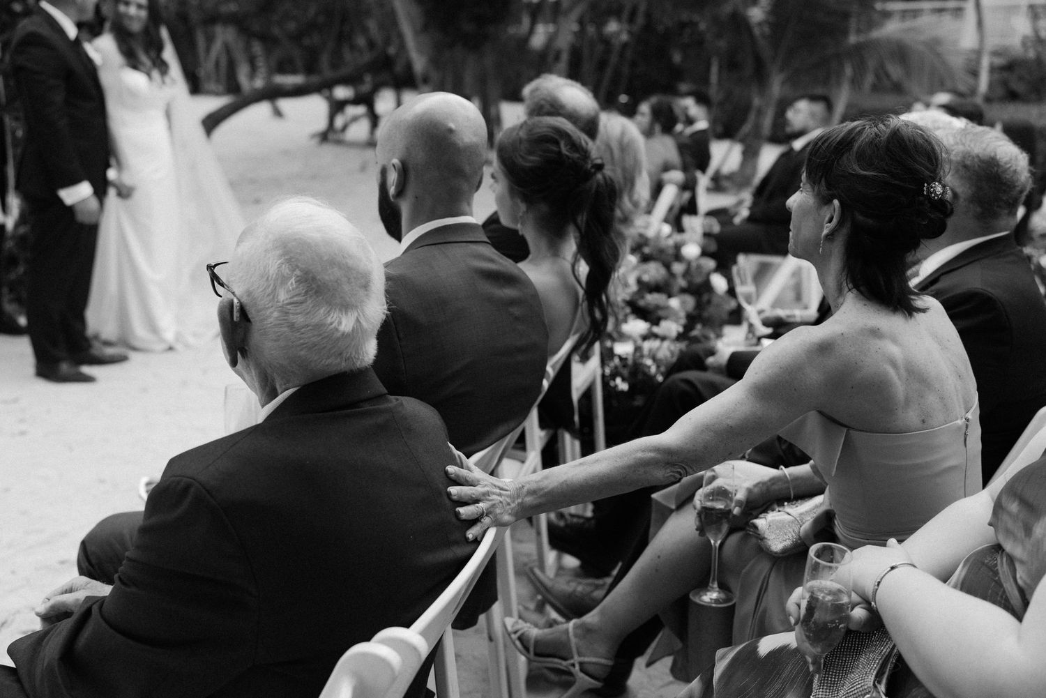 Wedding guests seated in rows capture photos during an outdoor ceremony.