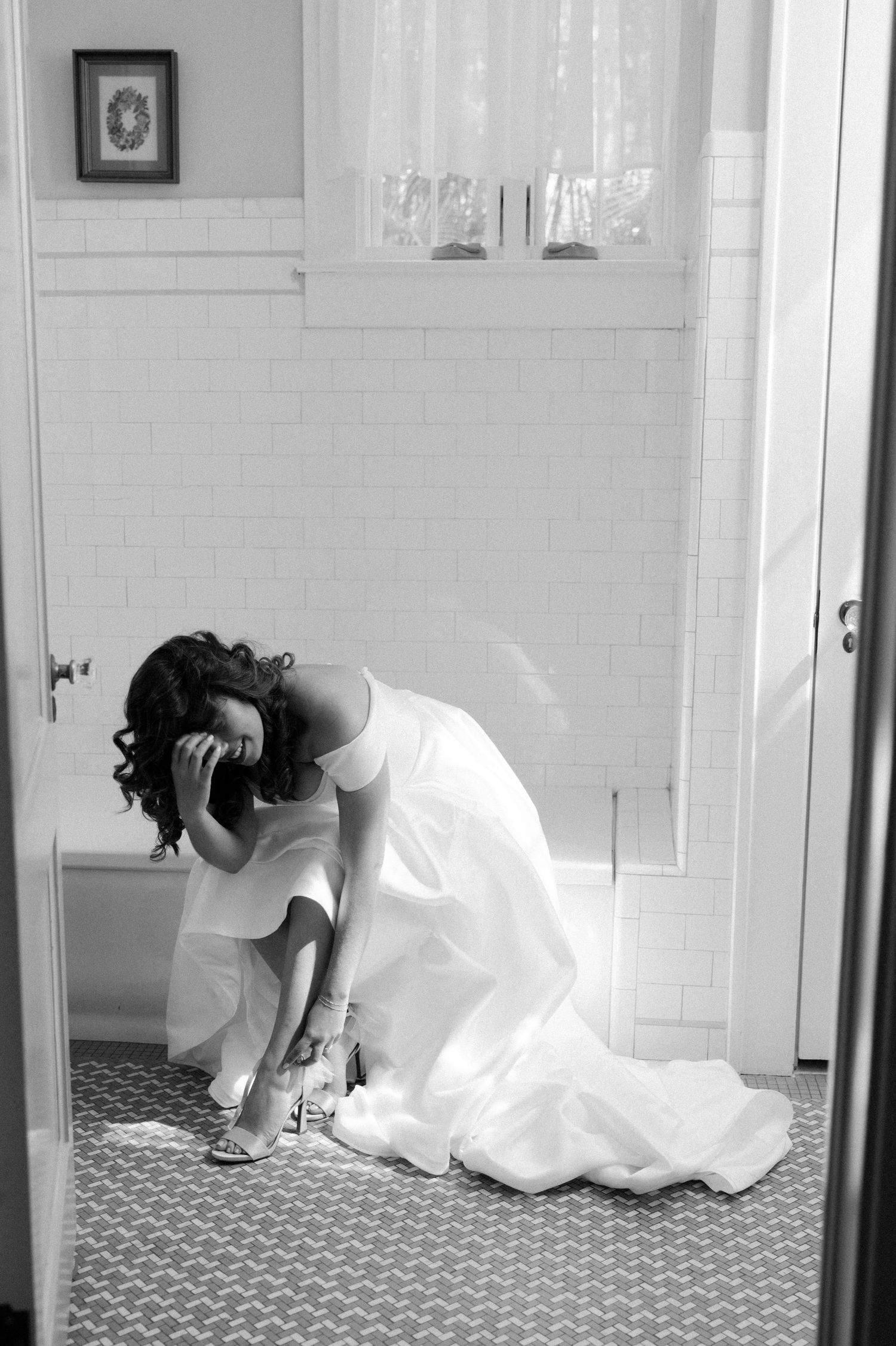 A person in a white wedding dress crouches on a patterned bathroom floor in a black and white photo.