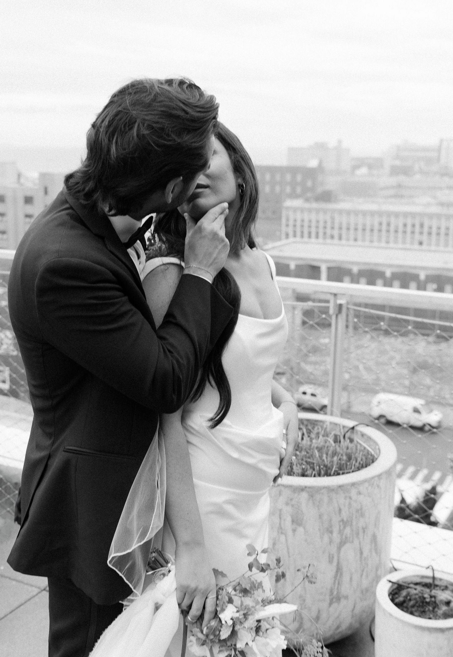 A romantic black and white moment shared between a couple on an urban balcony with city views.