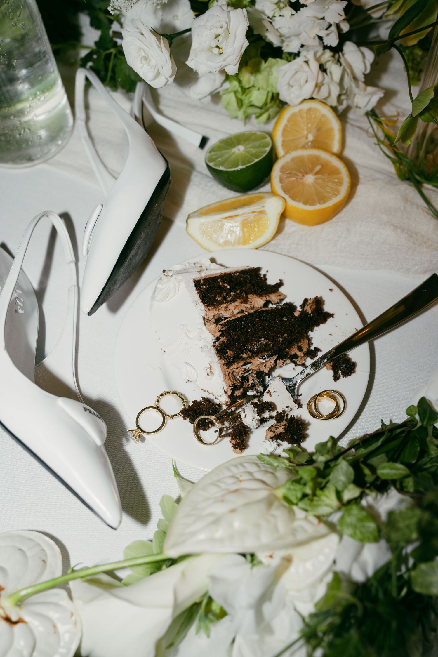 Wedding details with citrus slices, rings, and scattered cake crumbs on white tablecloth.