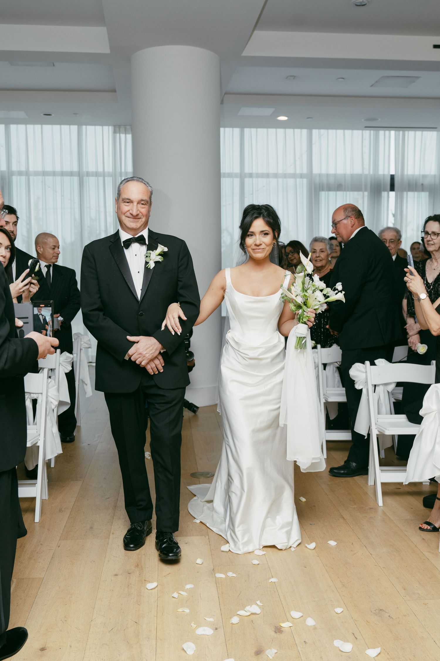 A couple walks down the aisle at their wedding ceremony while guests look on from white folding chairs.