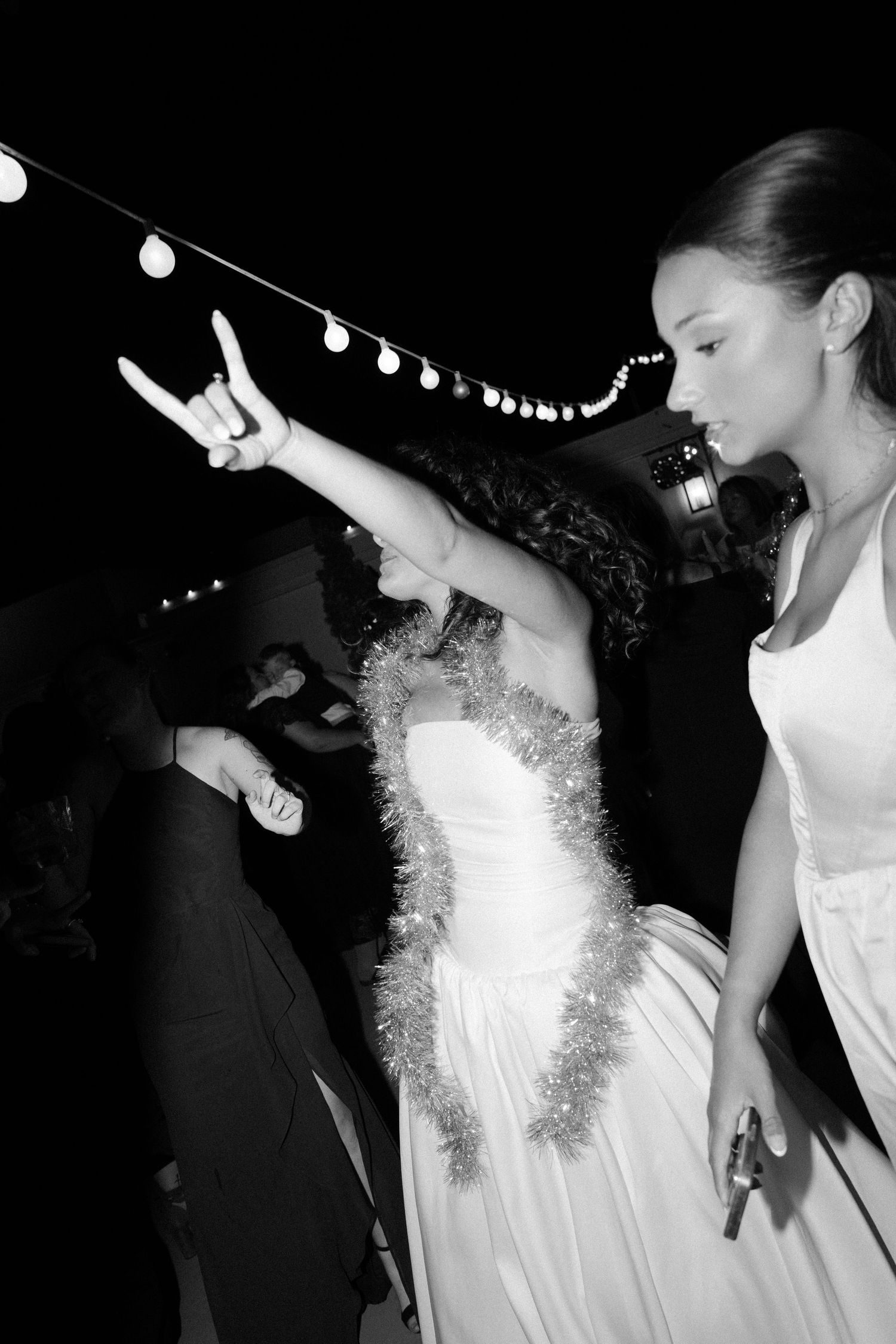 Black and white photo of dance floor celebration with string lights overhead.