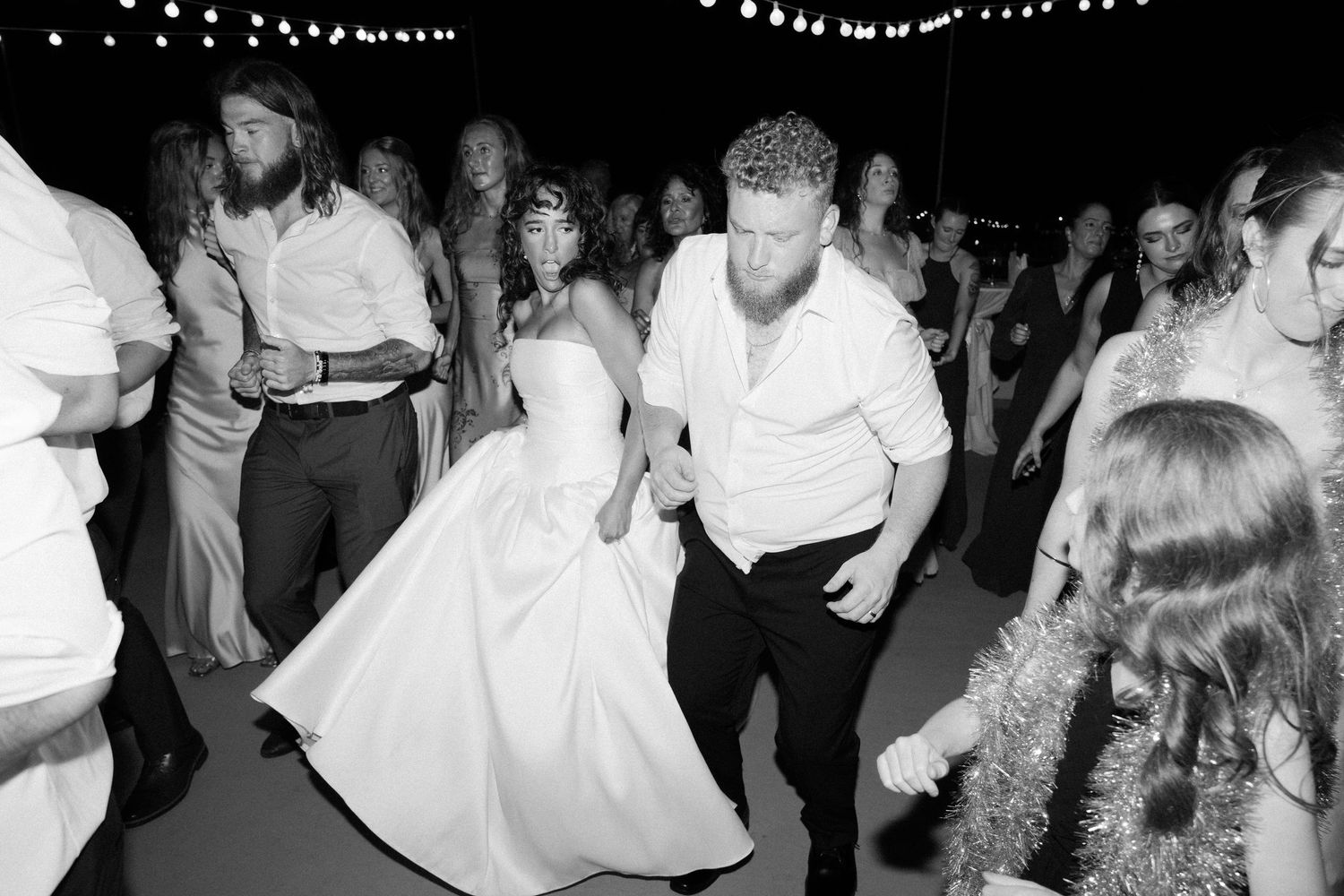 Wedding reception dance floor filled with guests celebrating under string lights.