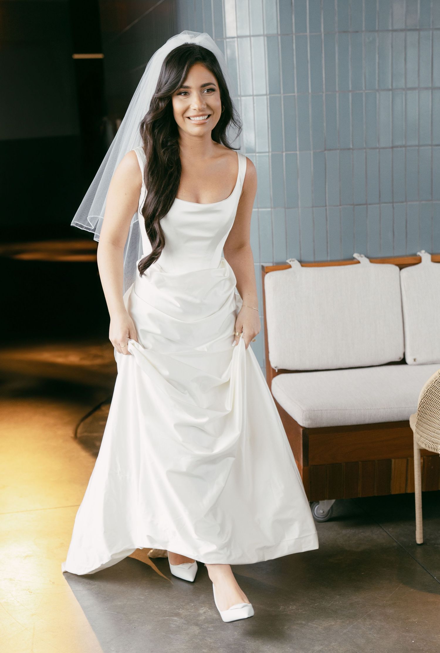 Woman wearing white sleeveless wedding dress posing in modern interior setting.