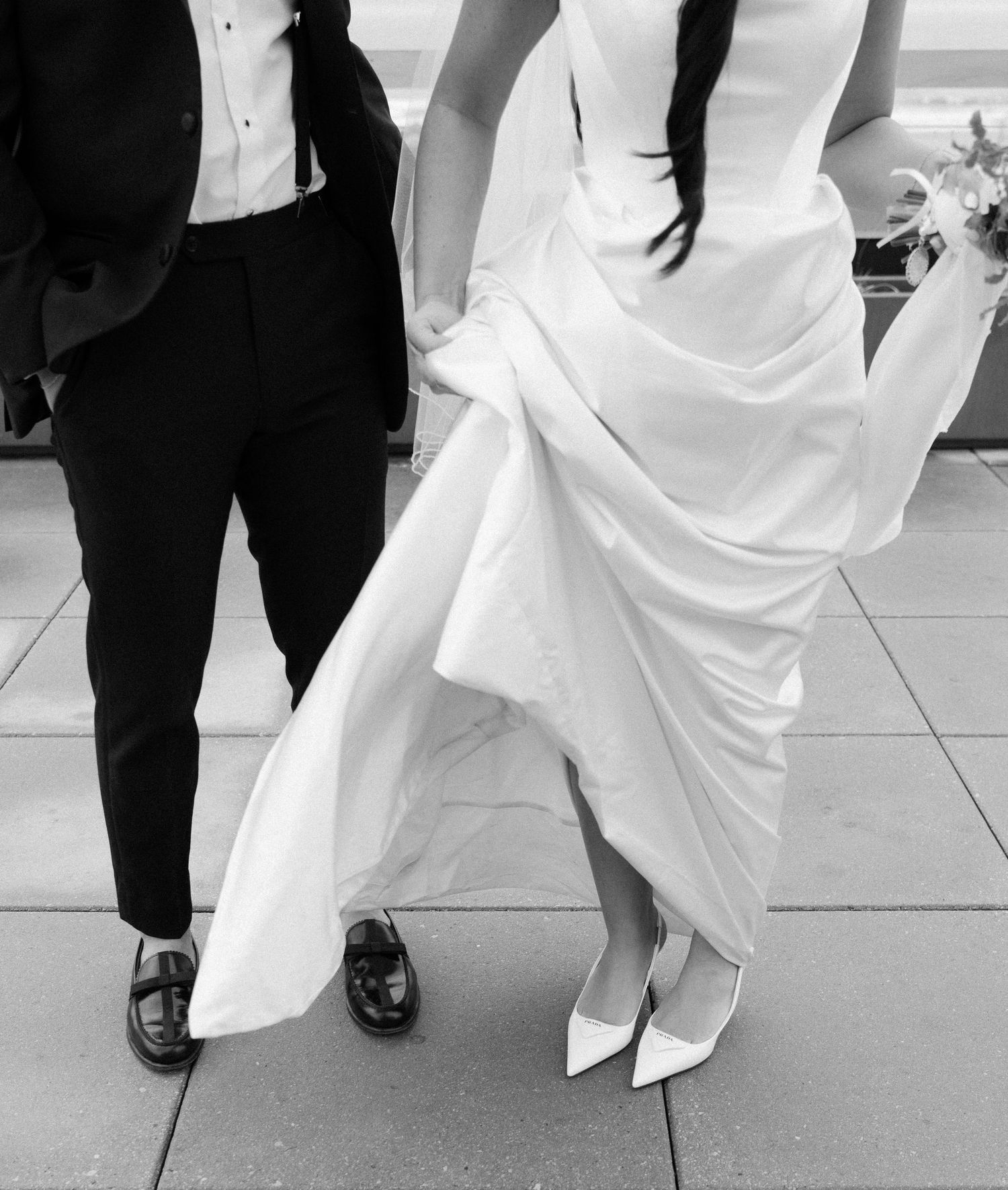 Close-up black and white photo of bride in white gown and groom in tuxedo showing their shoes while dancing.