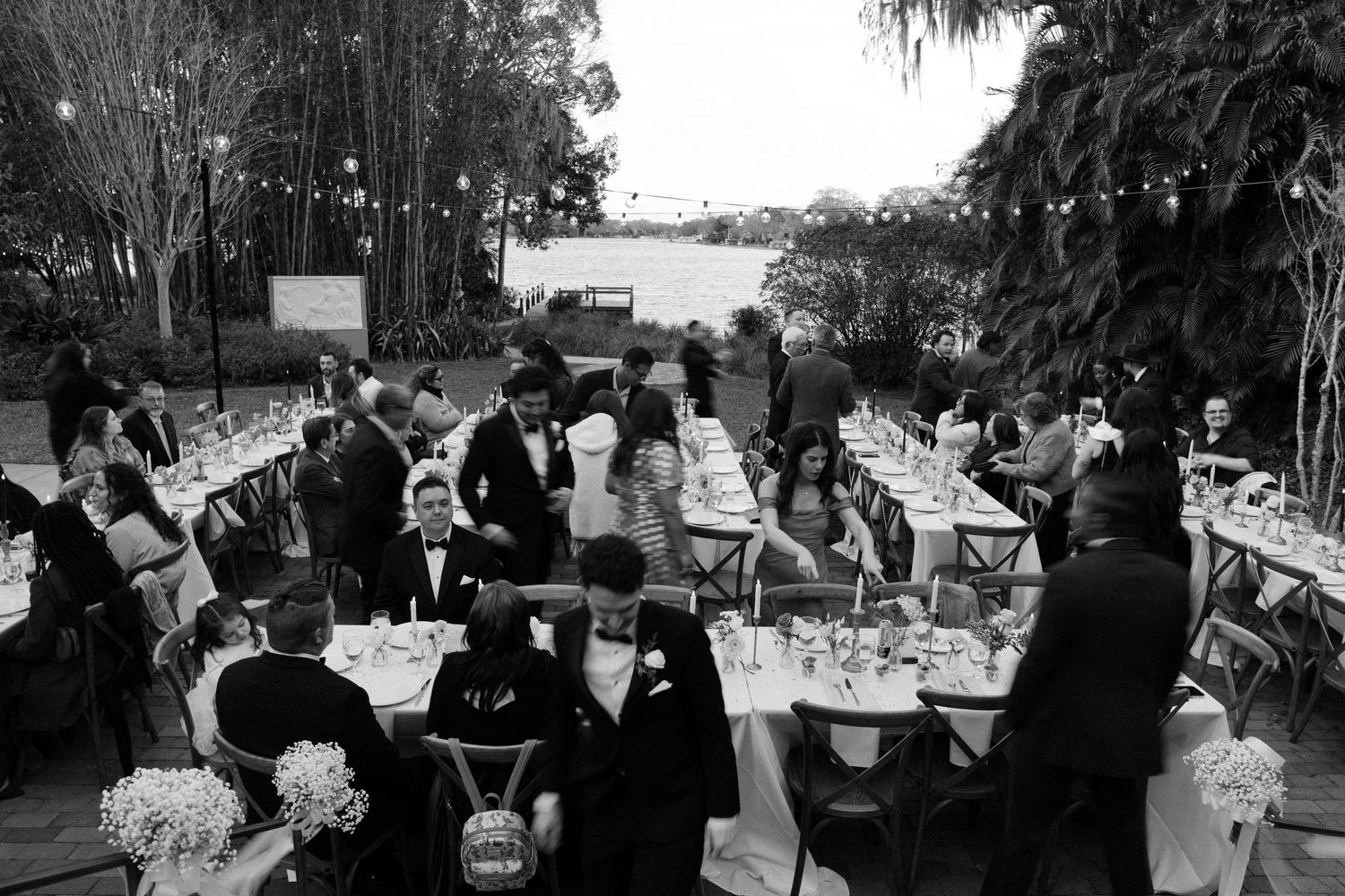 Black and white outdoor reception scene with tables and guests under a tent.