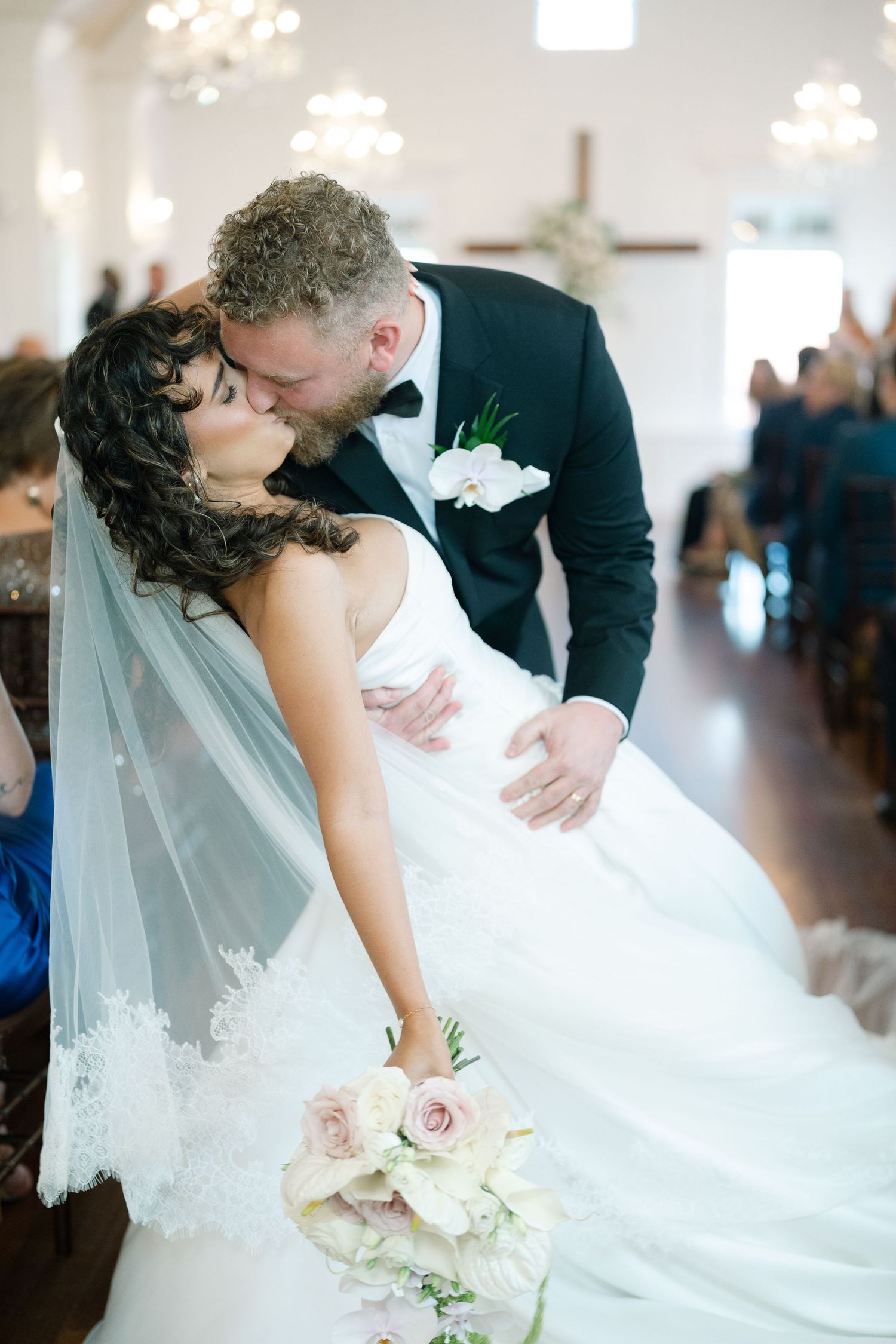 A romantic dip kiss moment at a wedding ceremony in an elegant church venue.